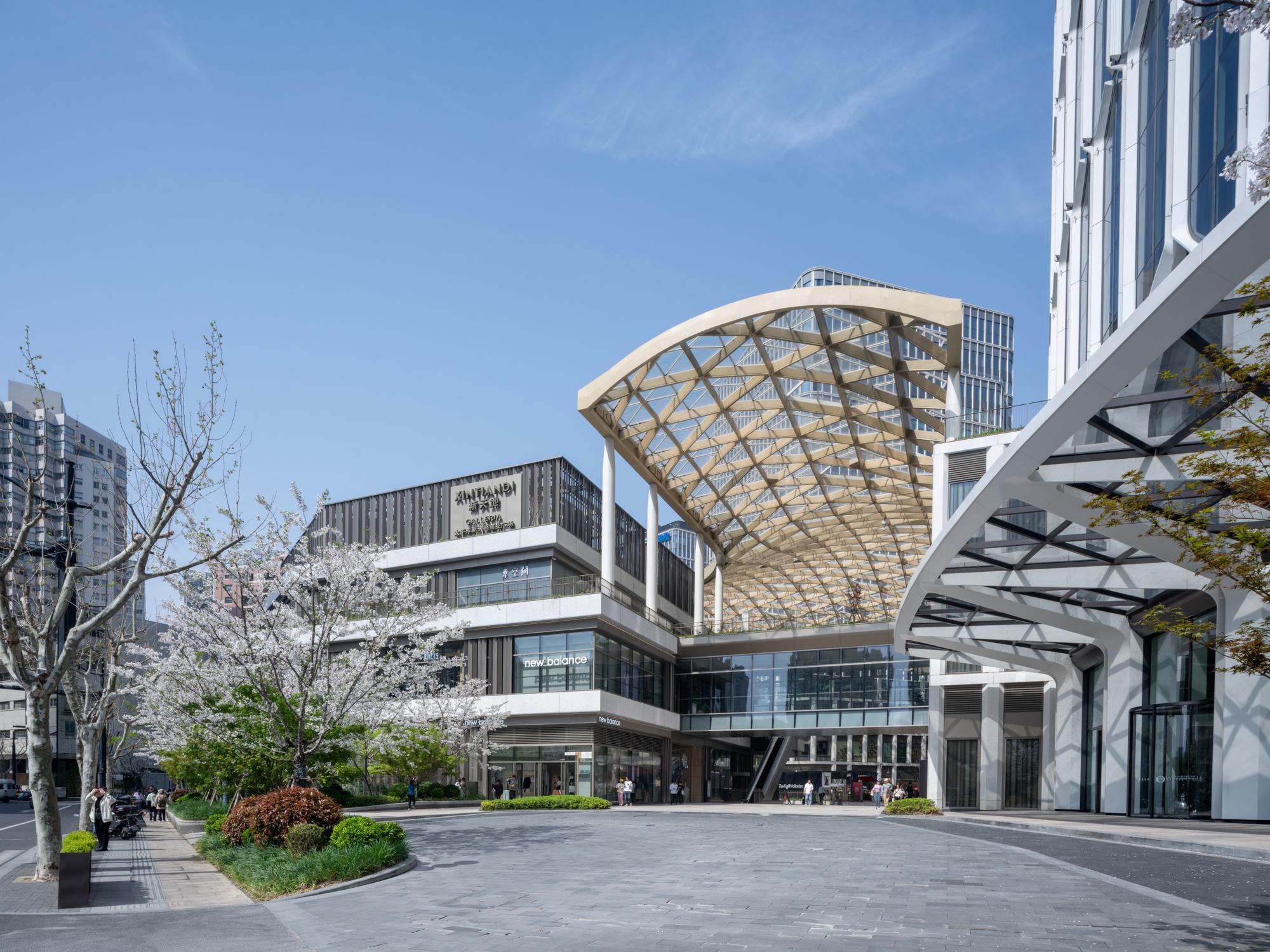 Exterior plaza view showing curved lattice roof canopy bridging between white facades under blue sky