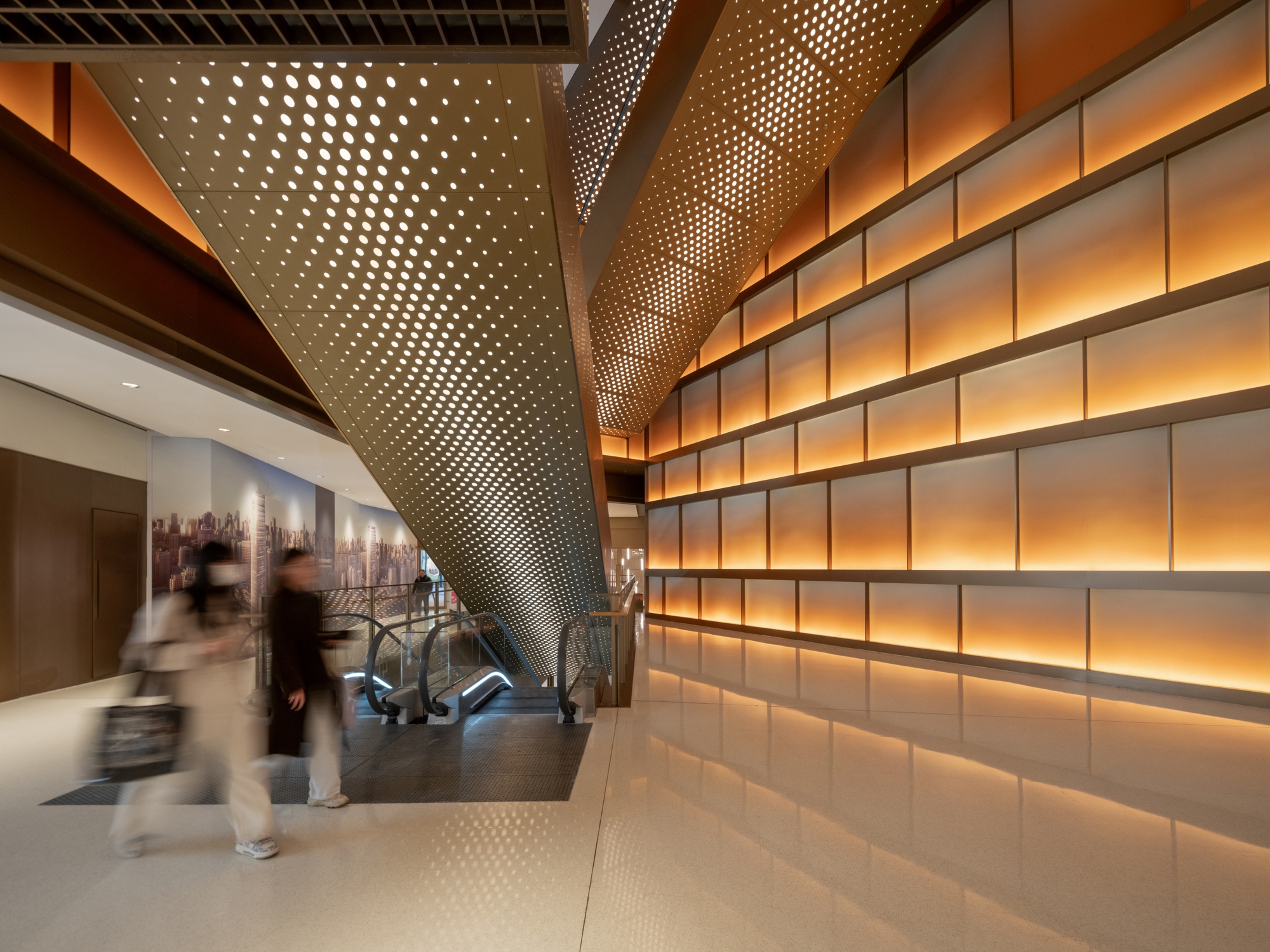 Interior corridor with perforated metal column and backlit horizontal panel wall as blurred figures pass by