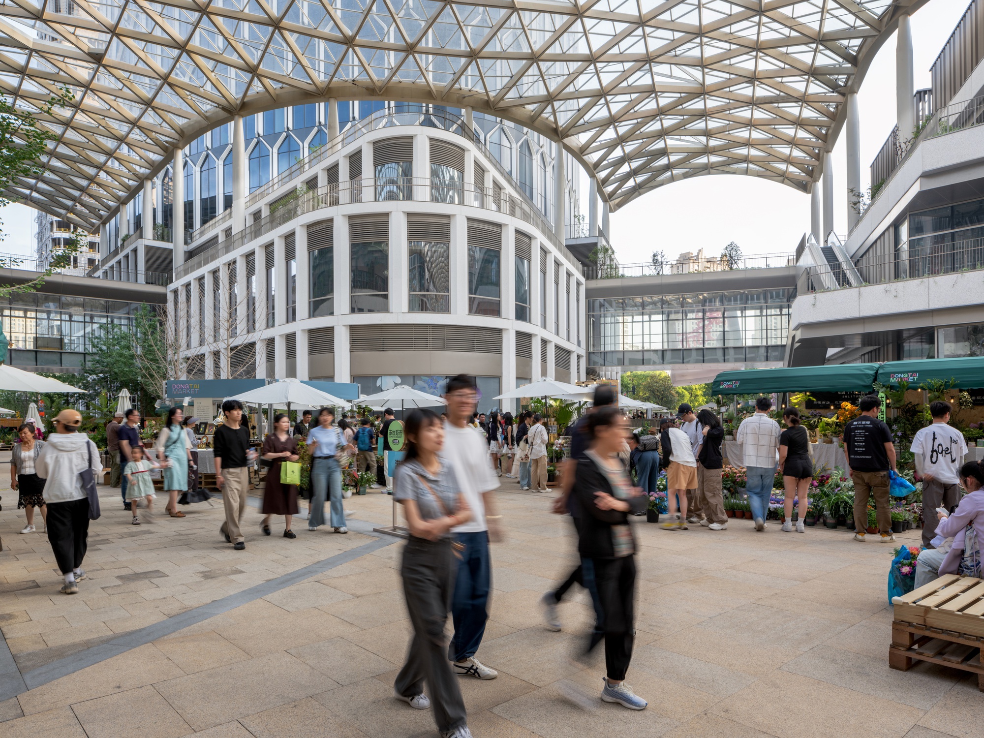 Covered market plaza with timber space frame roof and crowds moving through vendor stalls below