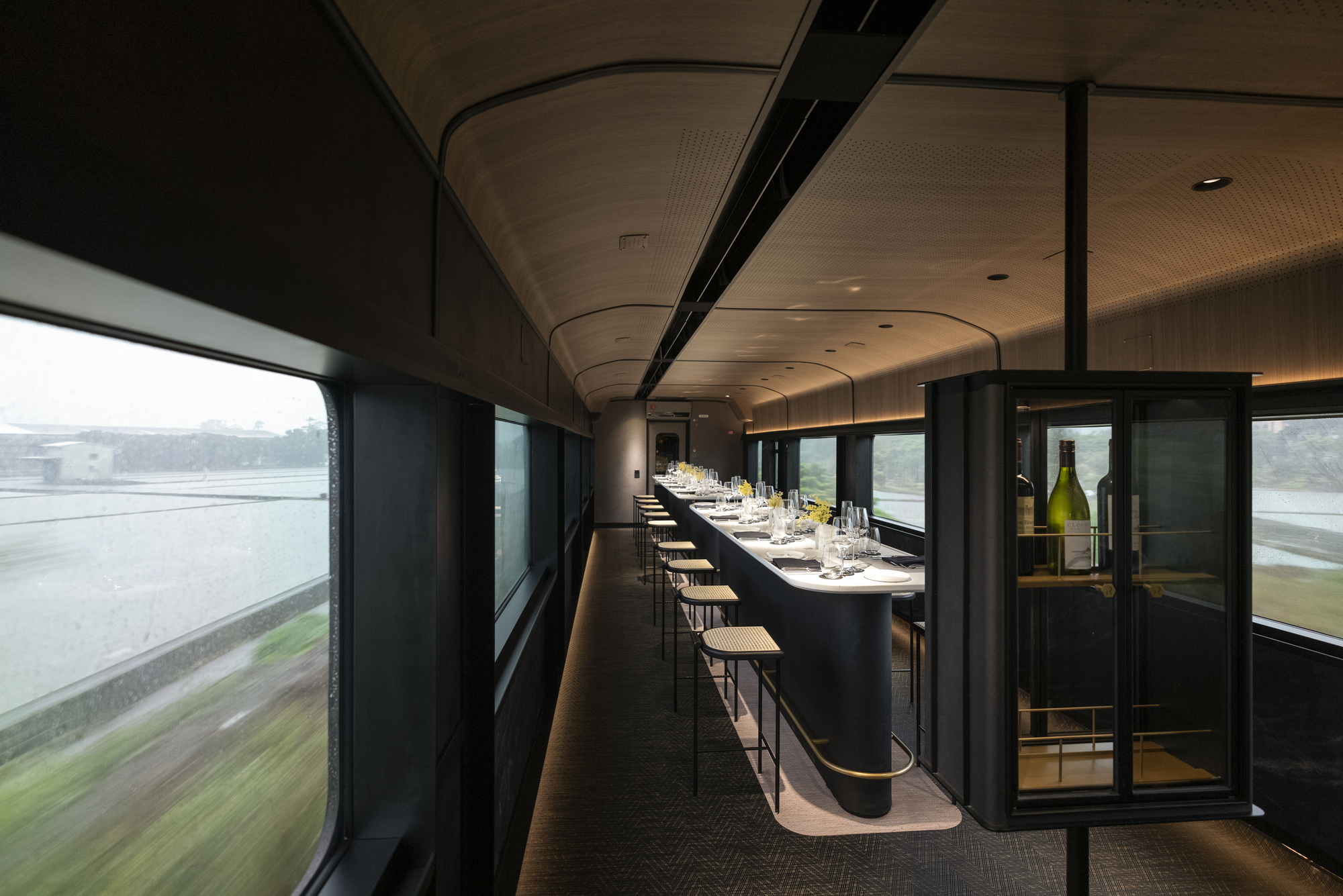 Interior dining car with curved timber ceiling, black banquette seating and landscape blurring past the windows