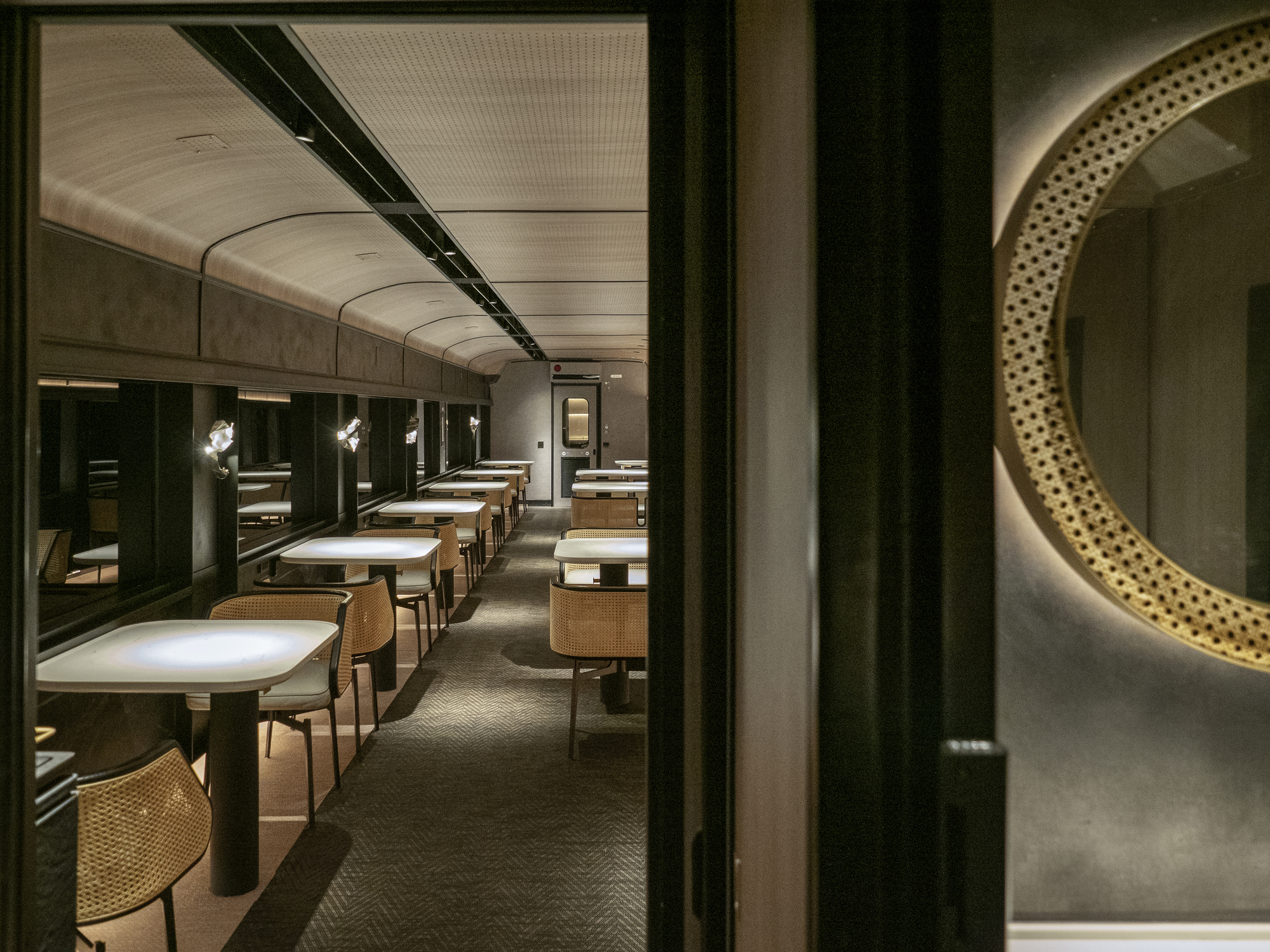 Long view down train dining carriage showing repeated booths beneath curved perforated ceiling