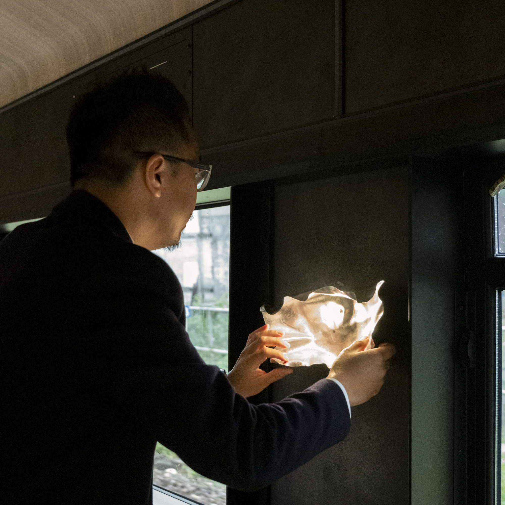 Passenger holding illuminated sculptural light fixture beside train window in darkened interior