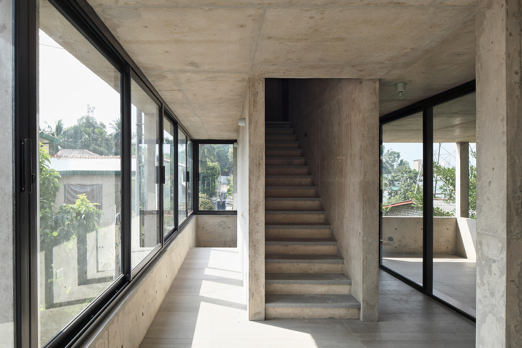 Freestanding concrete staircase flanked by floor-to-ceiling glazing in a sunlit interior