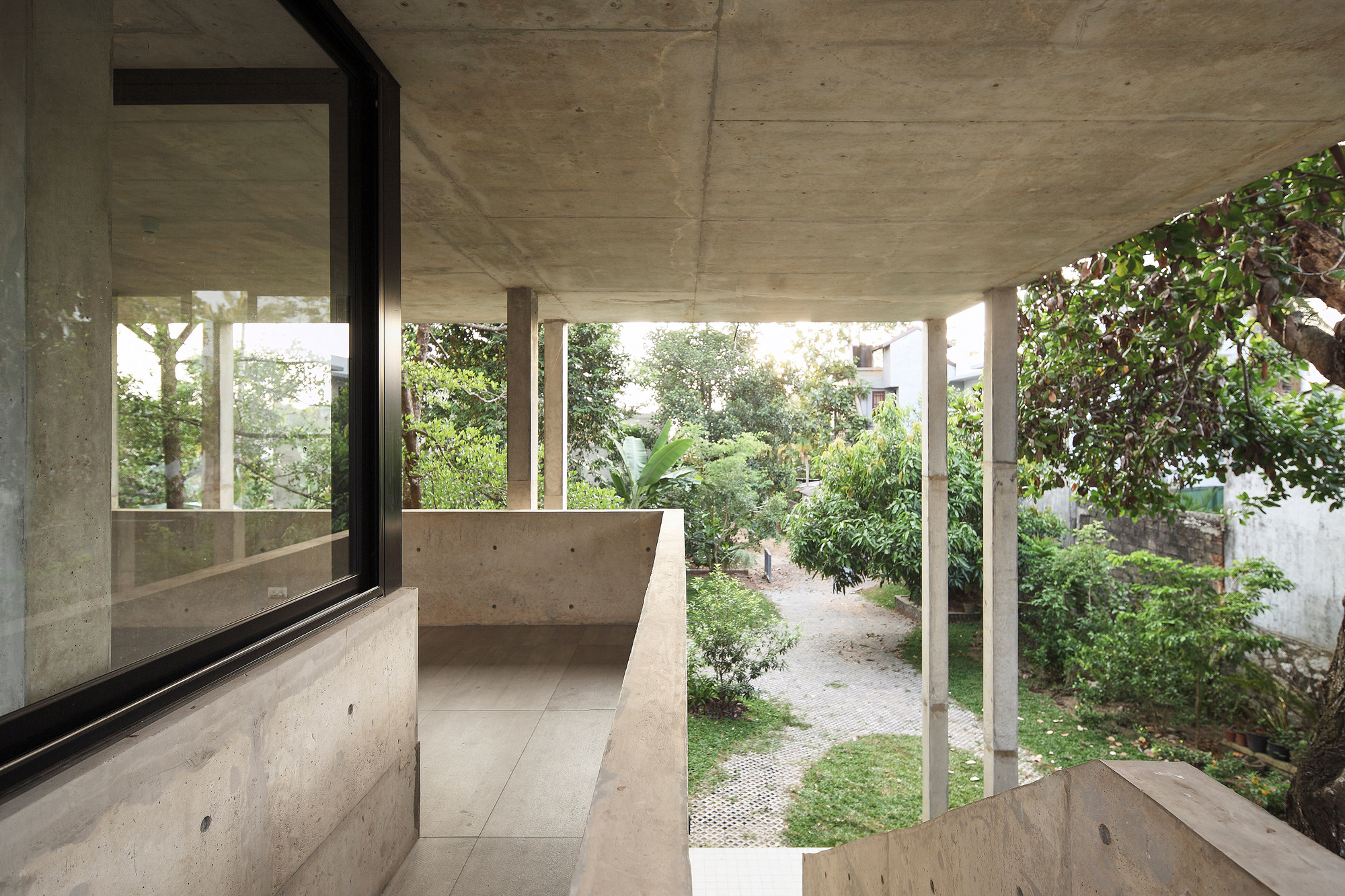 Covered balcony with concrete parapet overlooking a garden path and mature trees at dusk