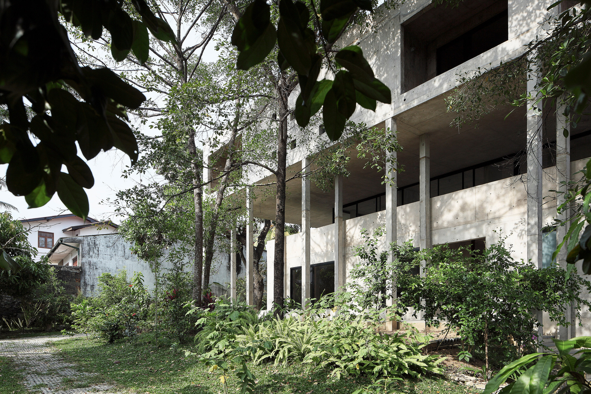 Elevated concrete structure on columns surrounded by mature trees and sloping garden