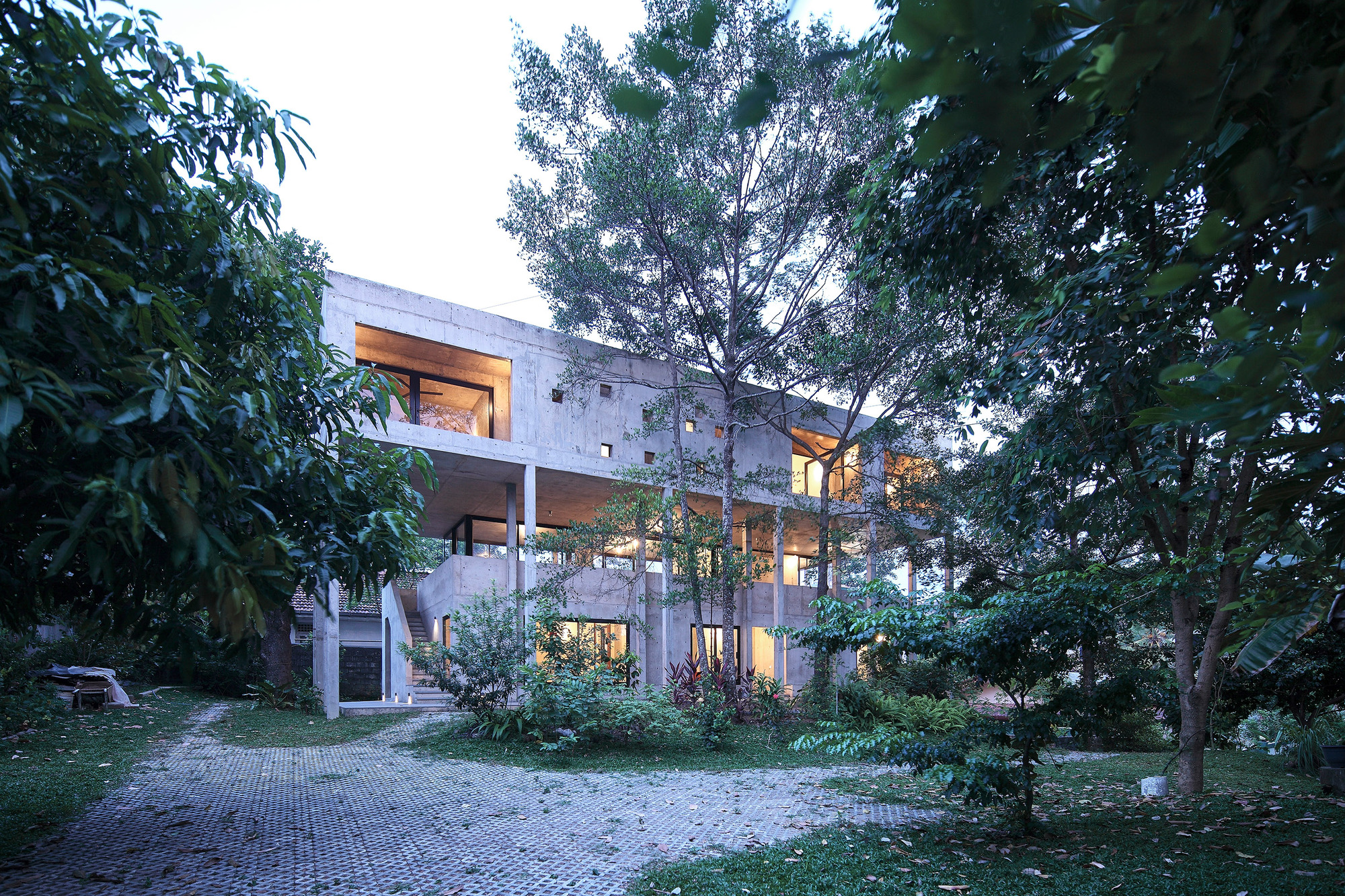 Garden view of the concrete house with recessed balconies amid mature trees at dusk