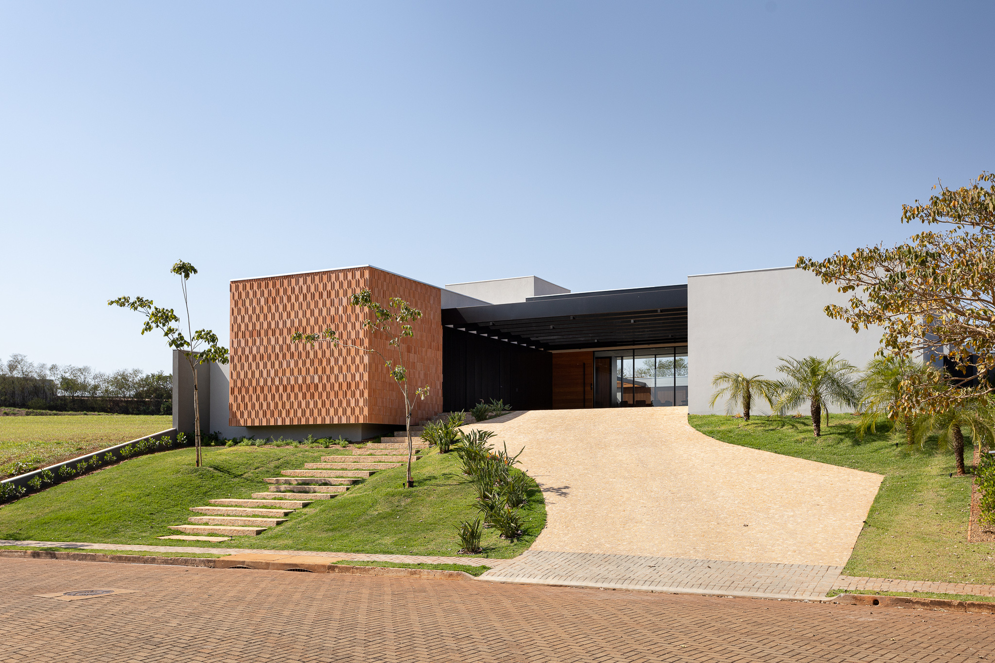 Front approach showing terracotta patterned screen wall, covered entry and gravel driveway flanked by planted beds