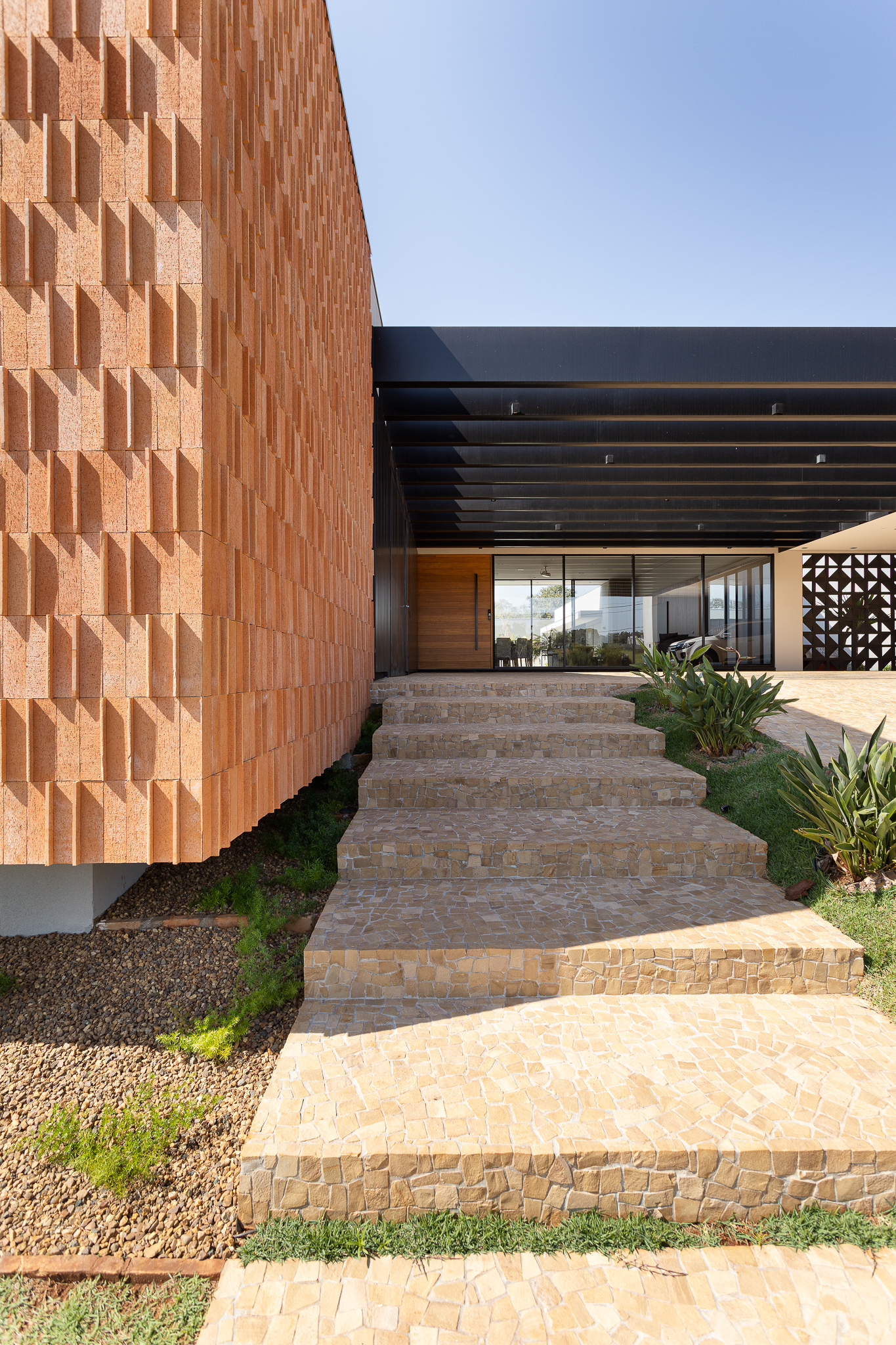 Entry walkway with stacked stone steps ascending past terracotta screen wall and planted agave specimens