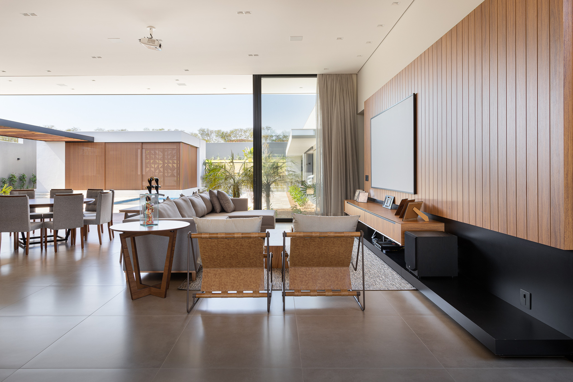 Living room with vertical timber wall paneling, large-format floor tiles, and full-height glazing framing the landscape