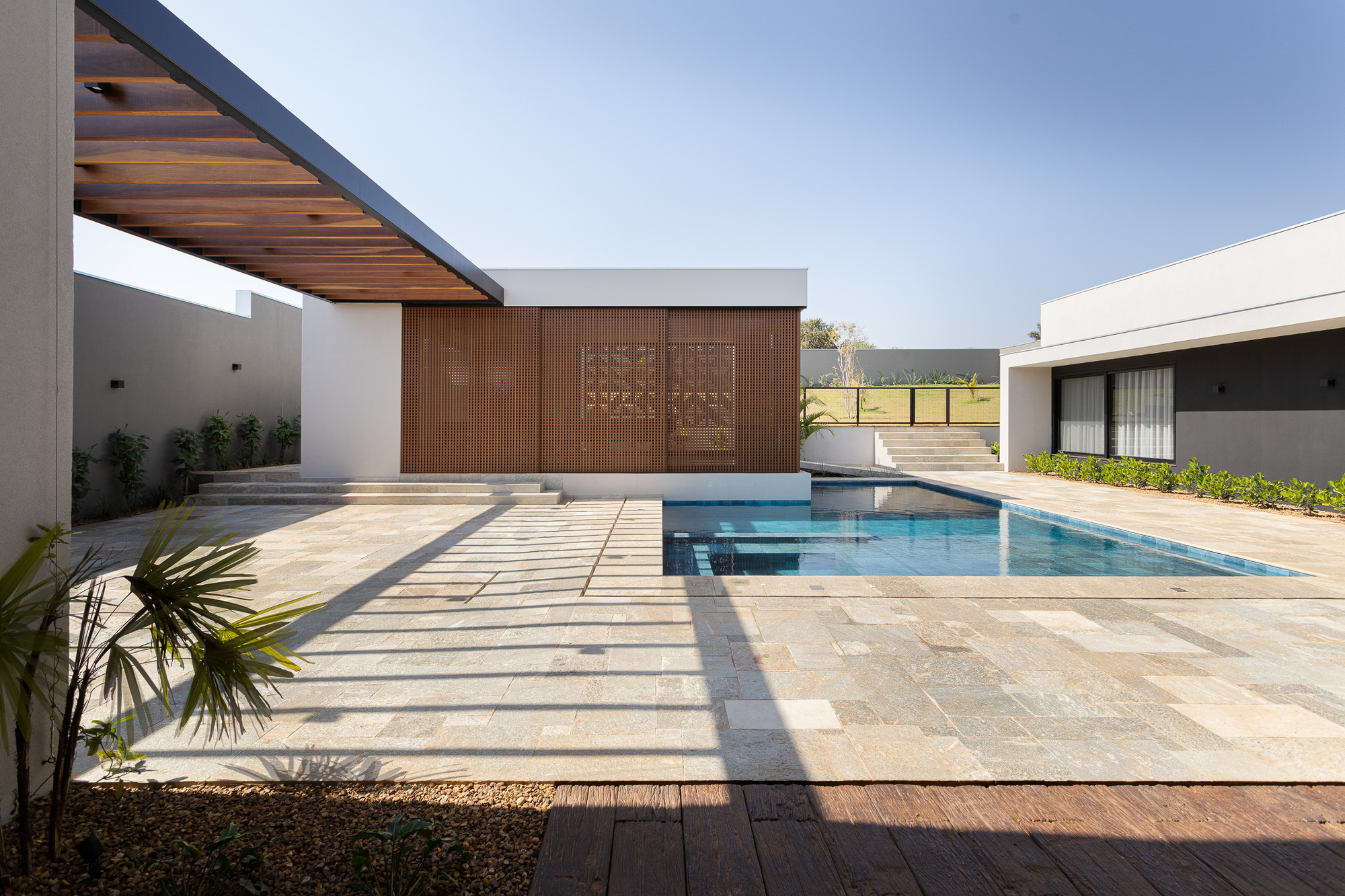 Courtyard view with patterned paving, timber deck inset, pool, slatted screen wall, and cantilevered timber soffit casting shadows