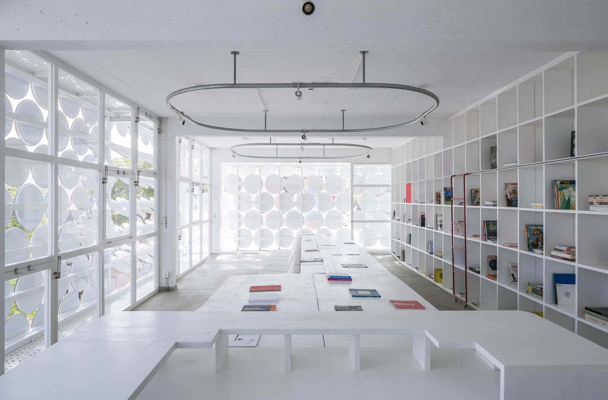 Interior reading room with white shelving, concrete floor, oval ceiling rails and daylight through perforated screens