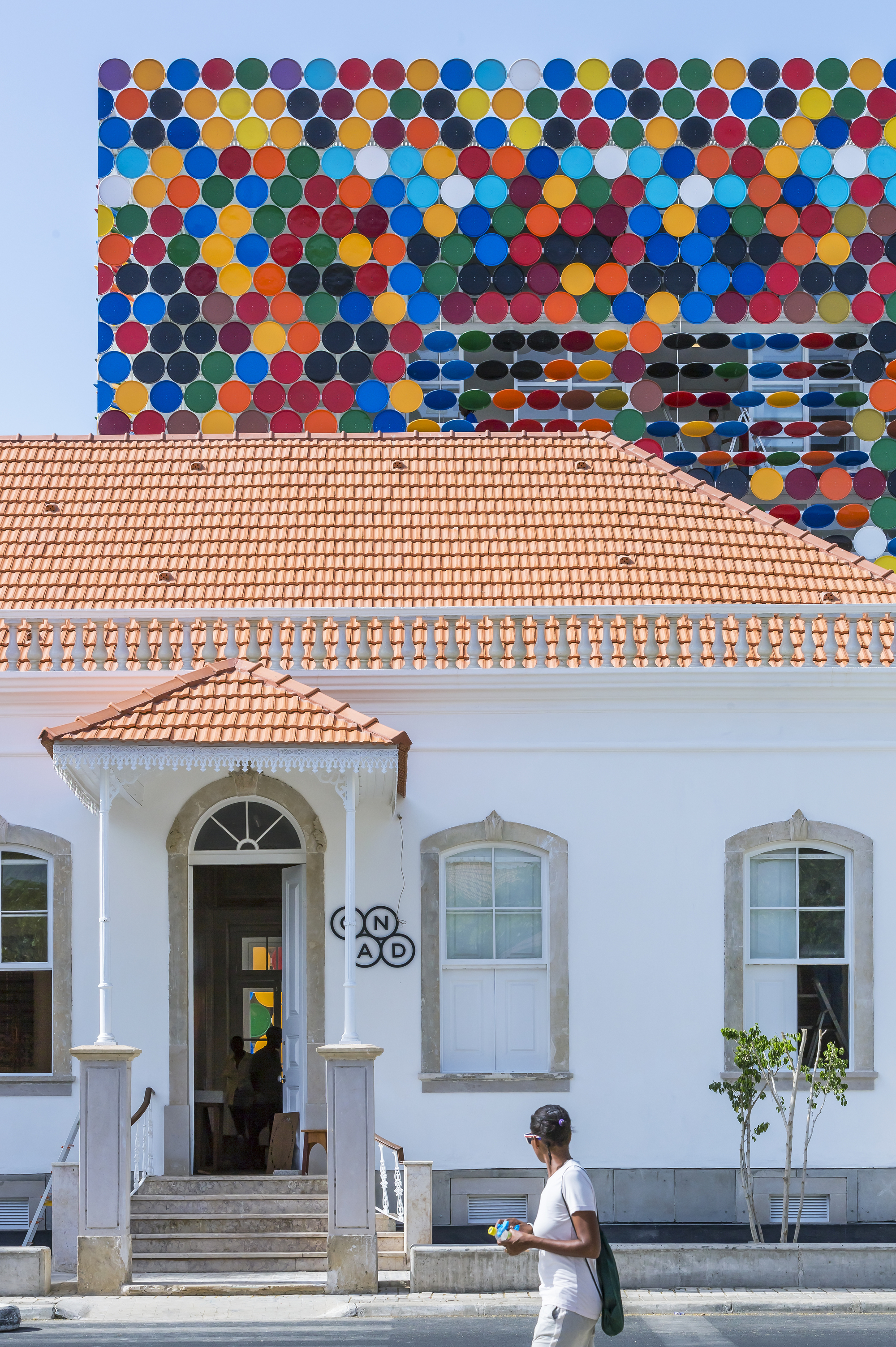Front elevation of the white building with terracotta roof and colourful disc backdrop at twilight