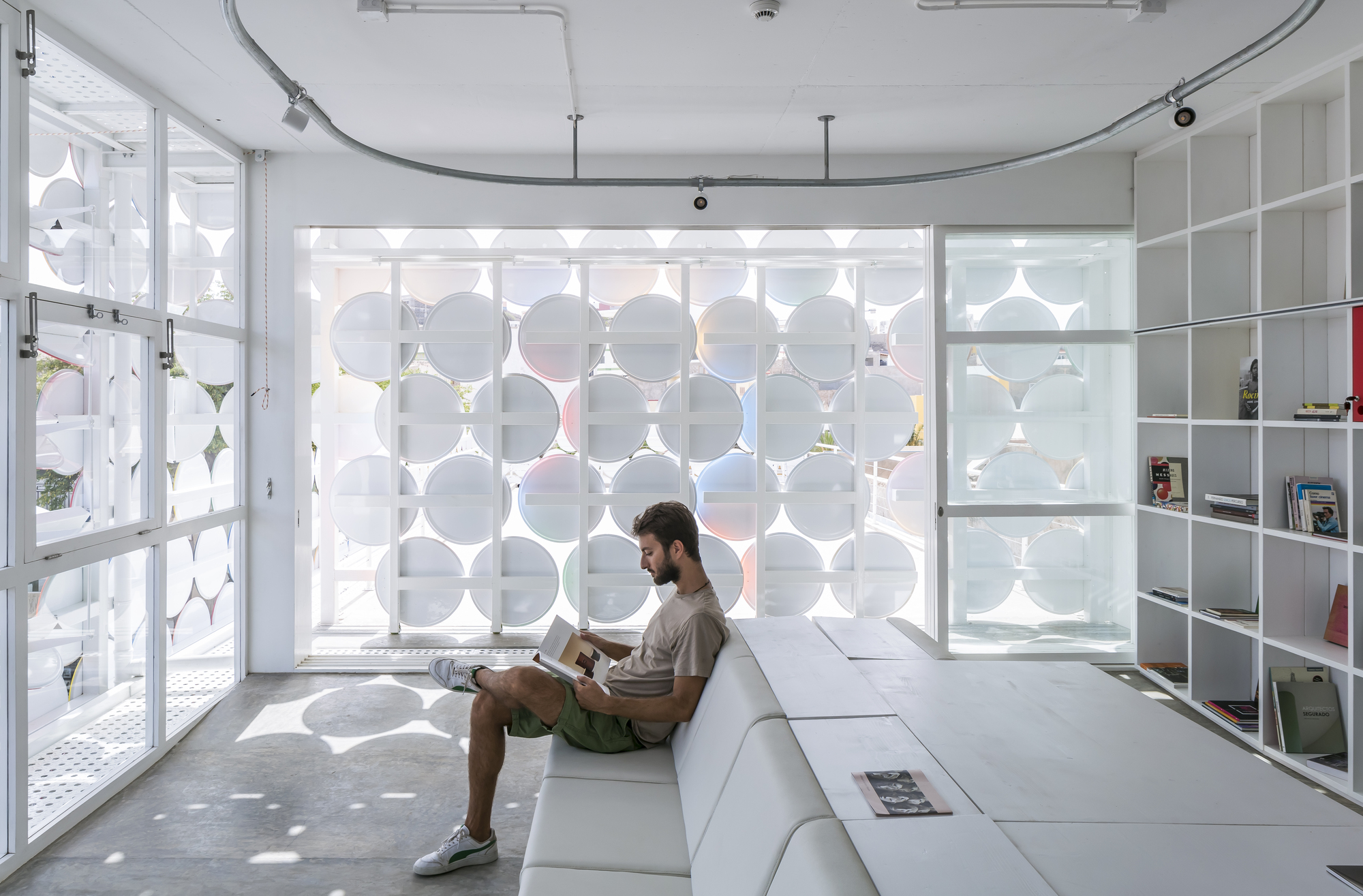 Interior room with circular patterned screen wall casting dappled shadows on a person seated on white platform