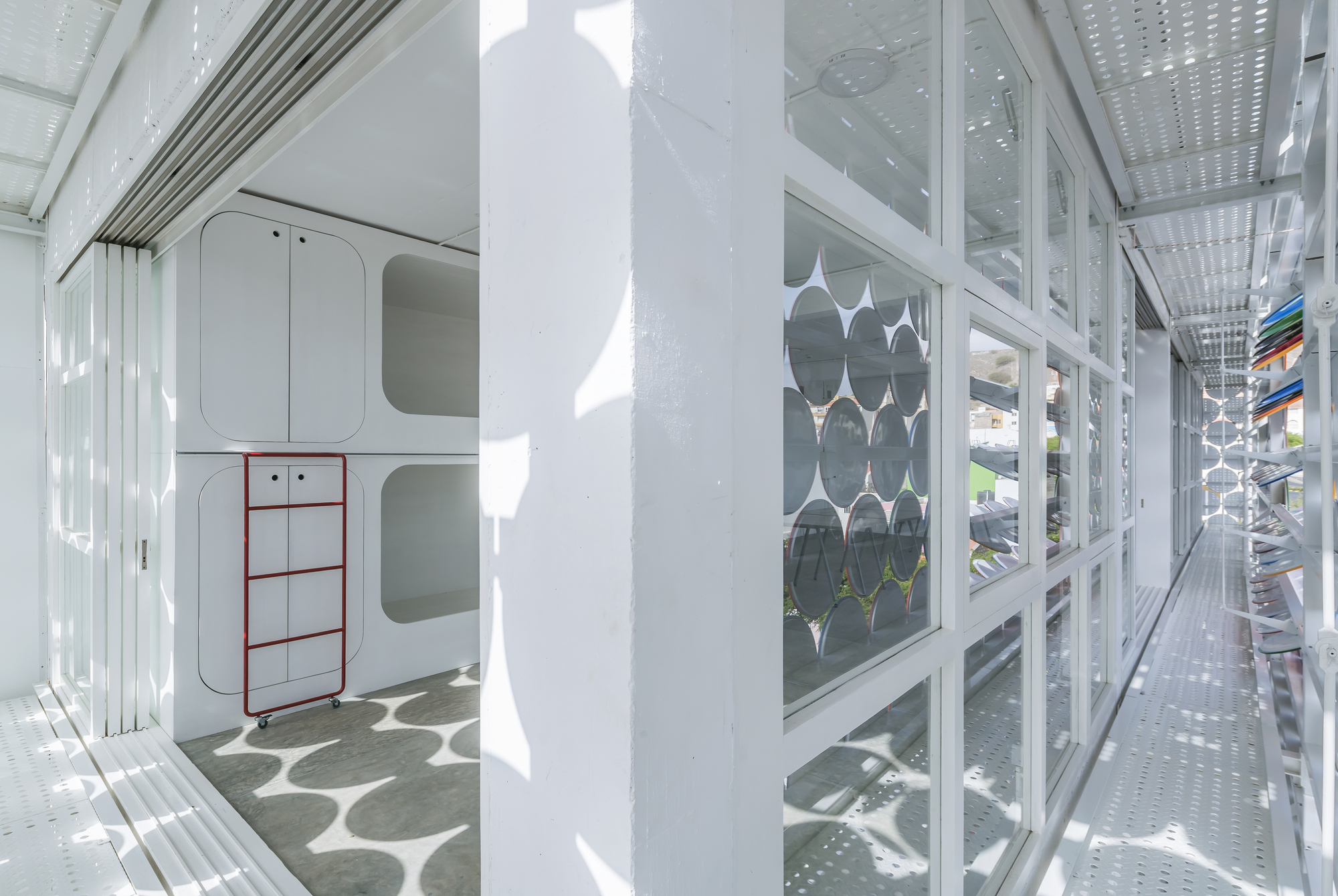 Narrow corridor with perforated metal ceiling and glazed wall overlooking the circular screen facade and plants