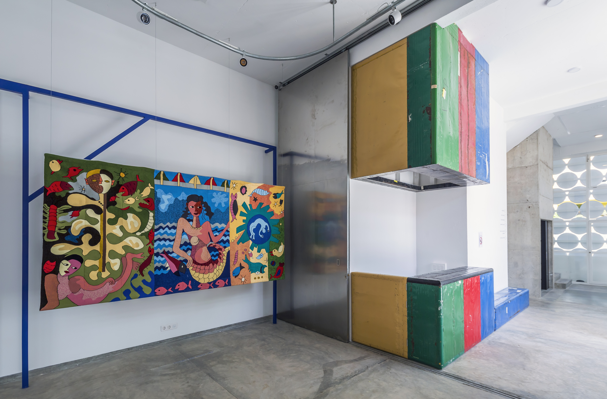 Gallery interior with multicolored striped kitchen volume beside concrete wall and blue steel frame
