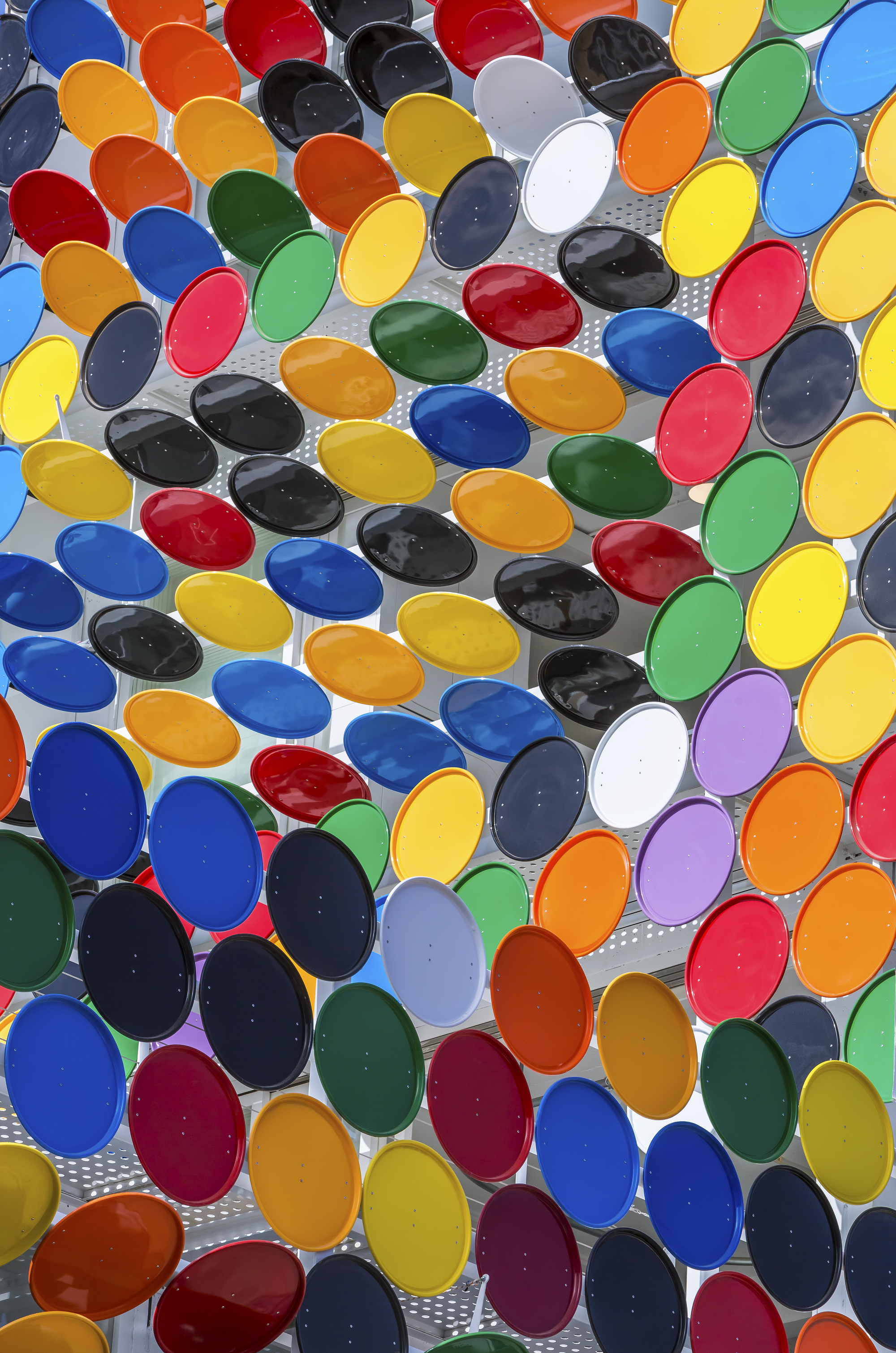 Close-up of multicolored oval glass lenses set in perforated metal screen in bright daylight