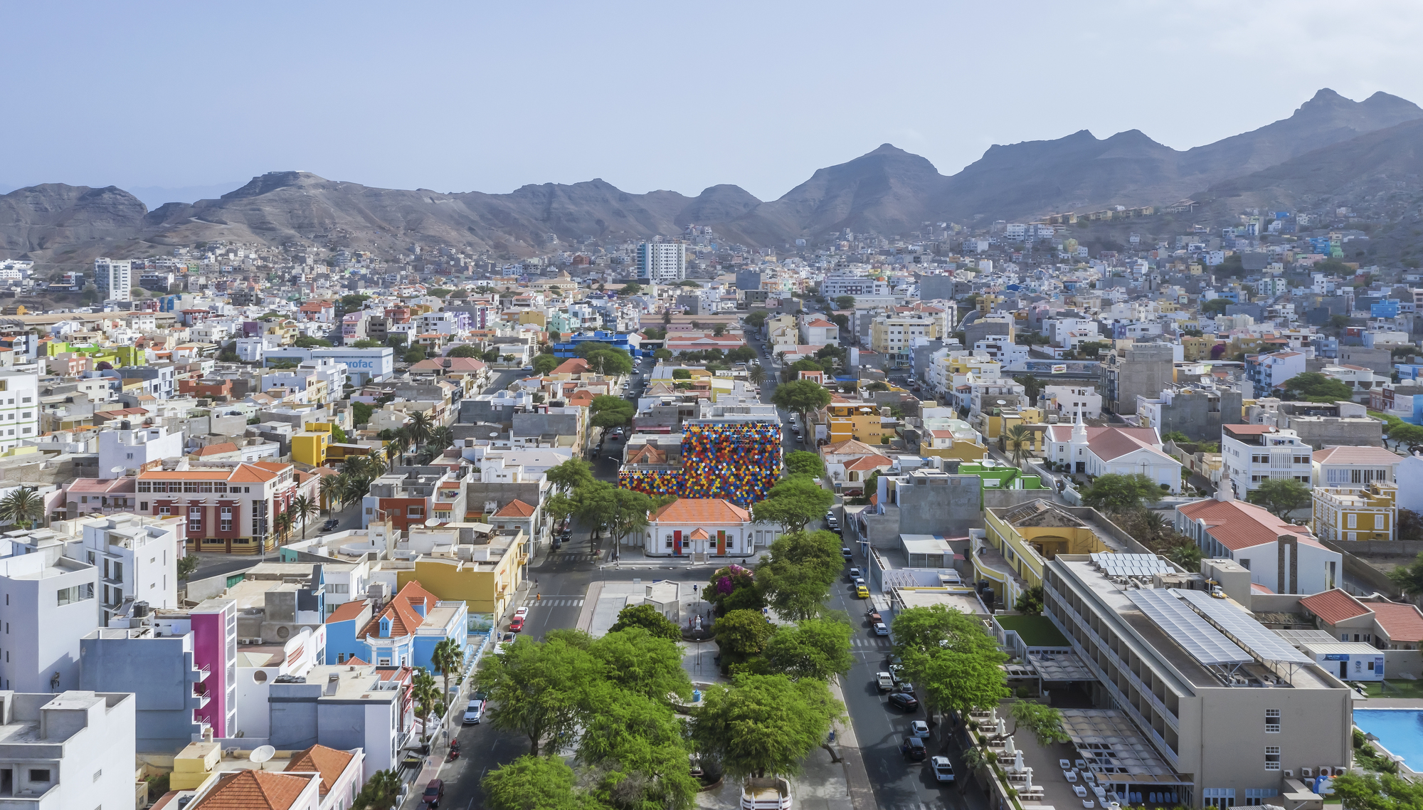 Distant aerial view showing the multicolored volume embedded within the hillside neighborhood fabric