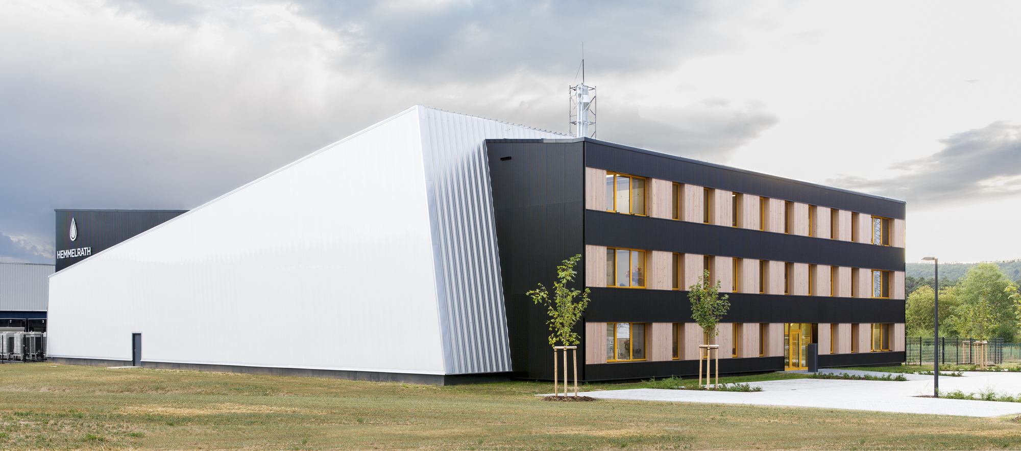 Corner view of white ribbed volume and black office wing with timber-framed windows under cloudy skies
