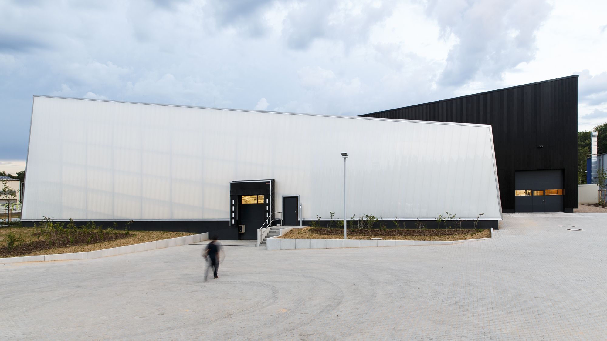 White ribbed facade wall with black framed entrance canopy and figure in motion crossing the pavement
