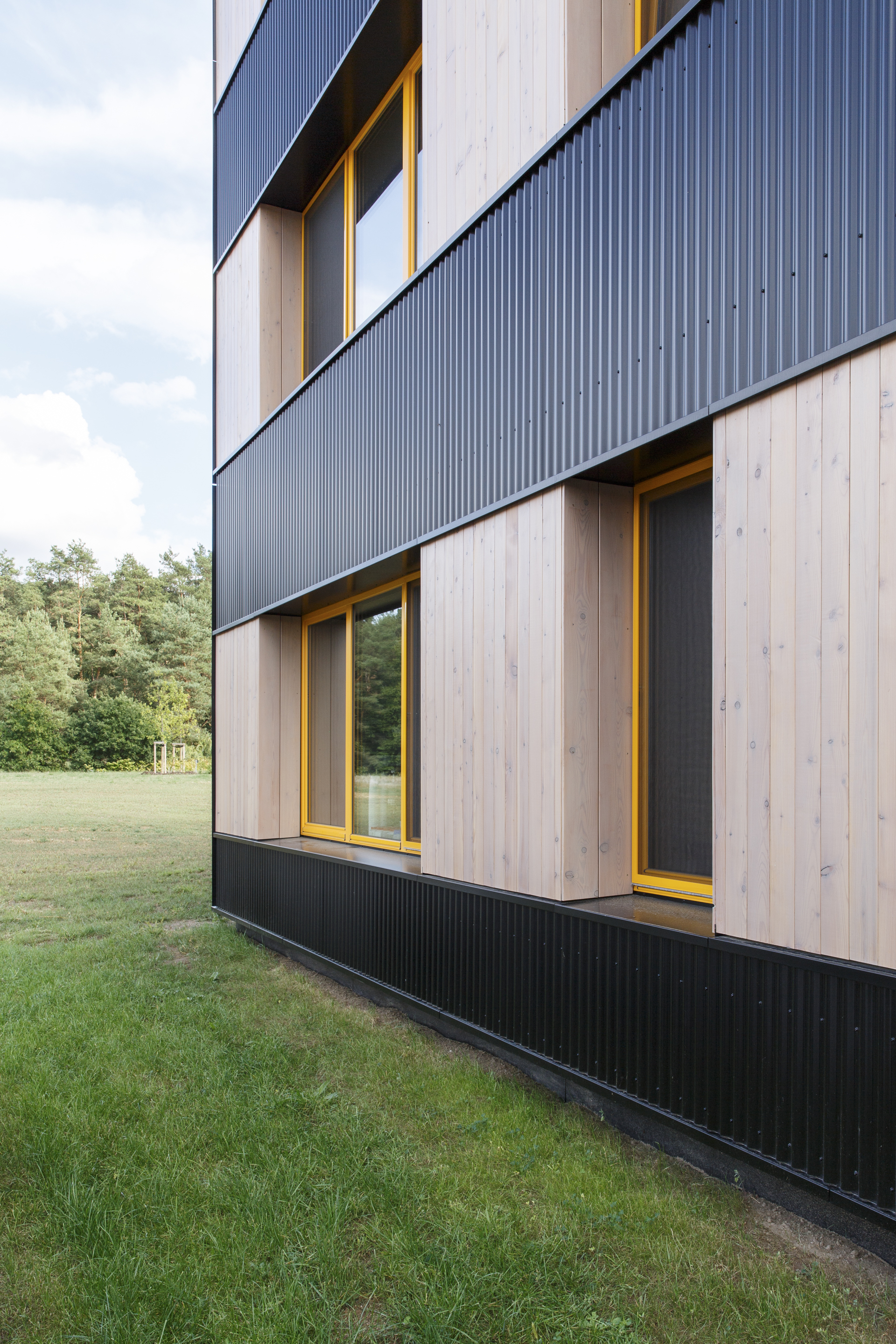 Side elevation showing alternating bands of dark metal cladding and light timber with yellow-framed windows