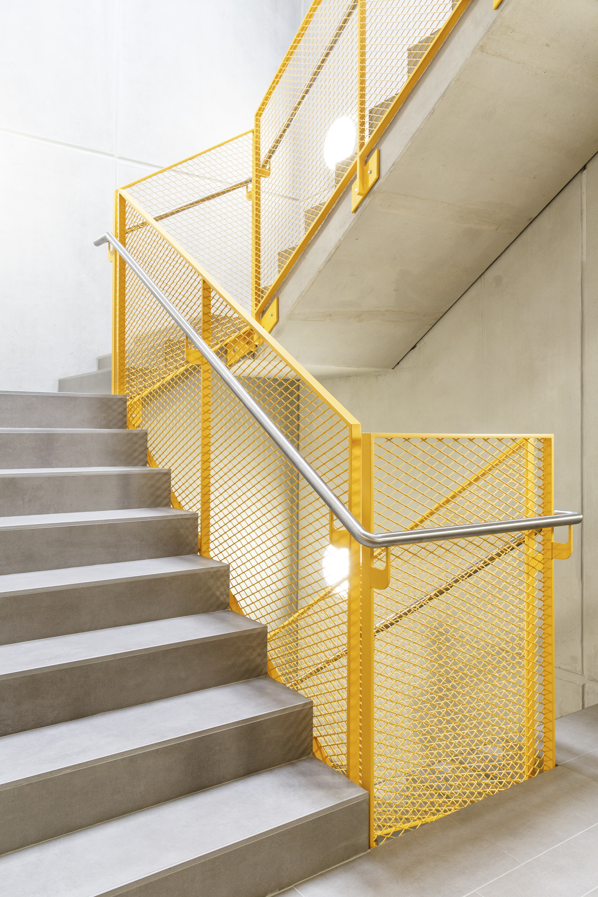 Concrete staircase with yellow powder-coated steel mesh balustrades and a stainless steel handrail
