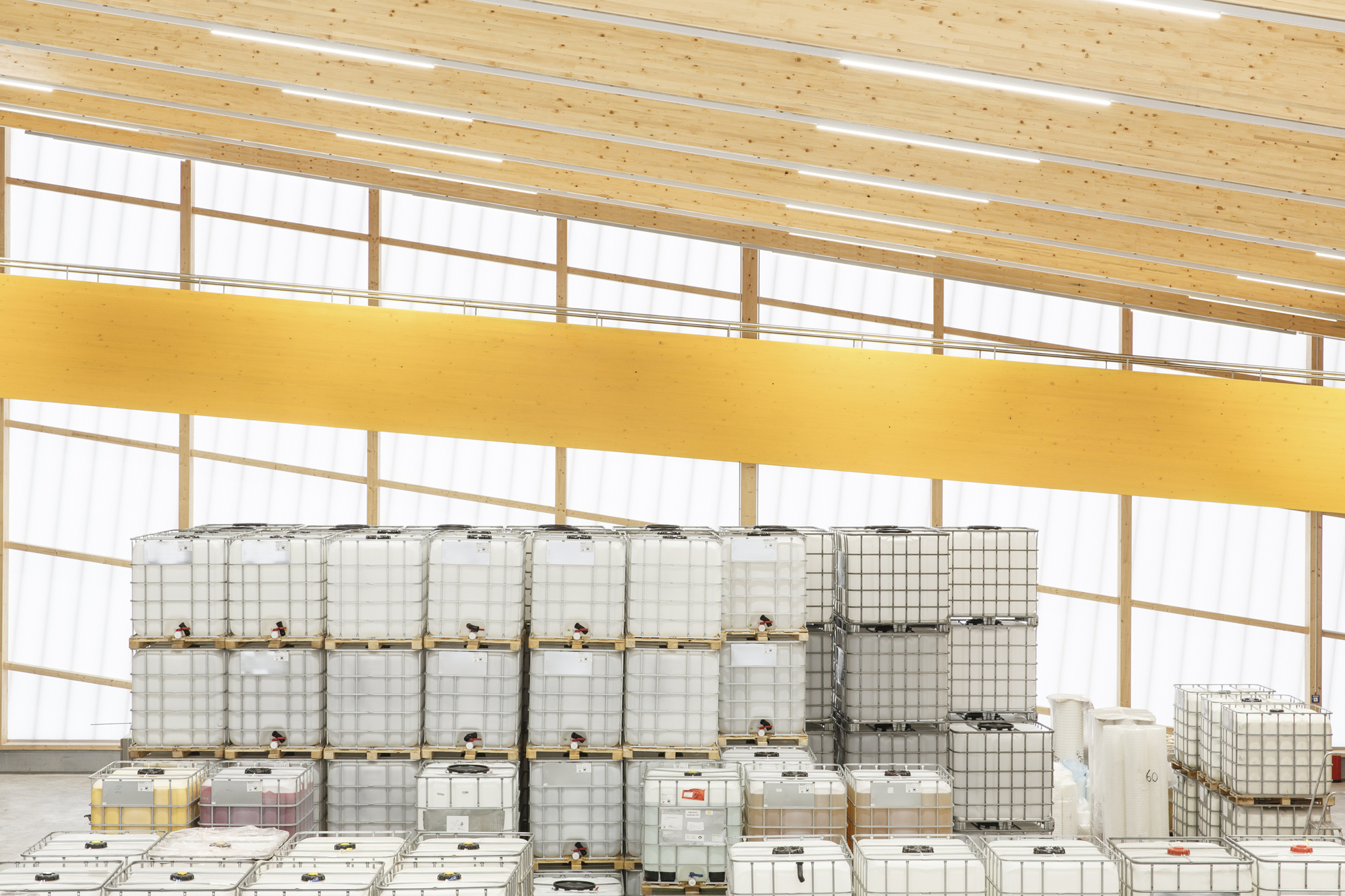 Interior view of industrial storage area with white plastic containers stacked below a yellow mezzanine and timber ceiling