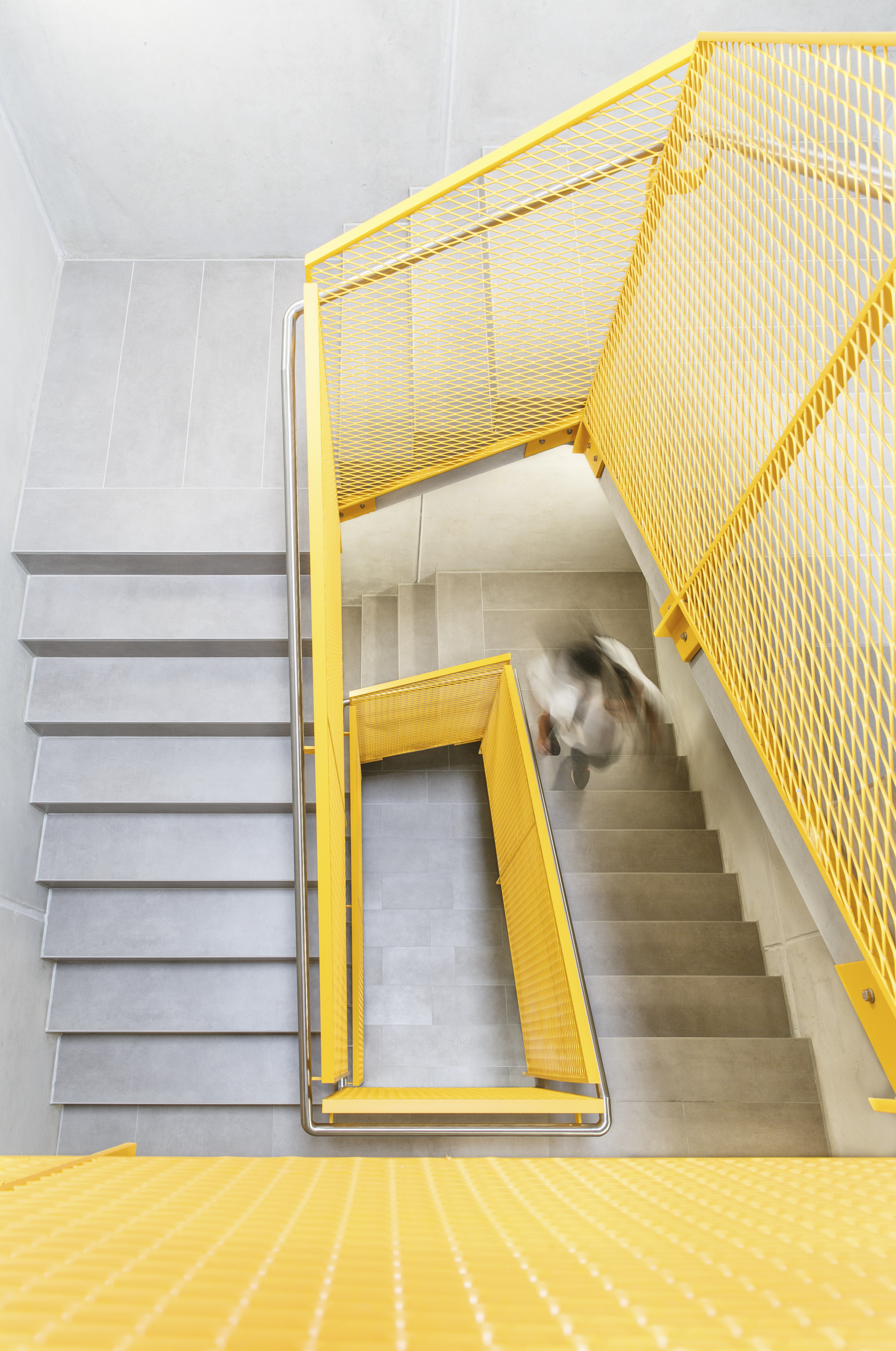 Top-down view of yellow metal mesh stairwell with a person descending the concrete steps