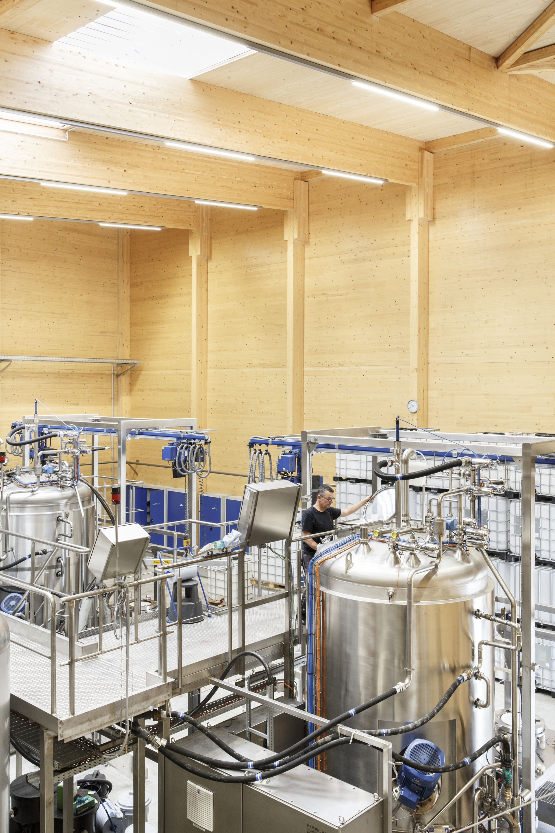 Production space with steel brewing tanks and platforms beneath exposed timber beams and linear lighting