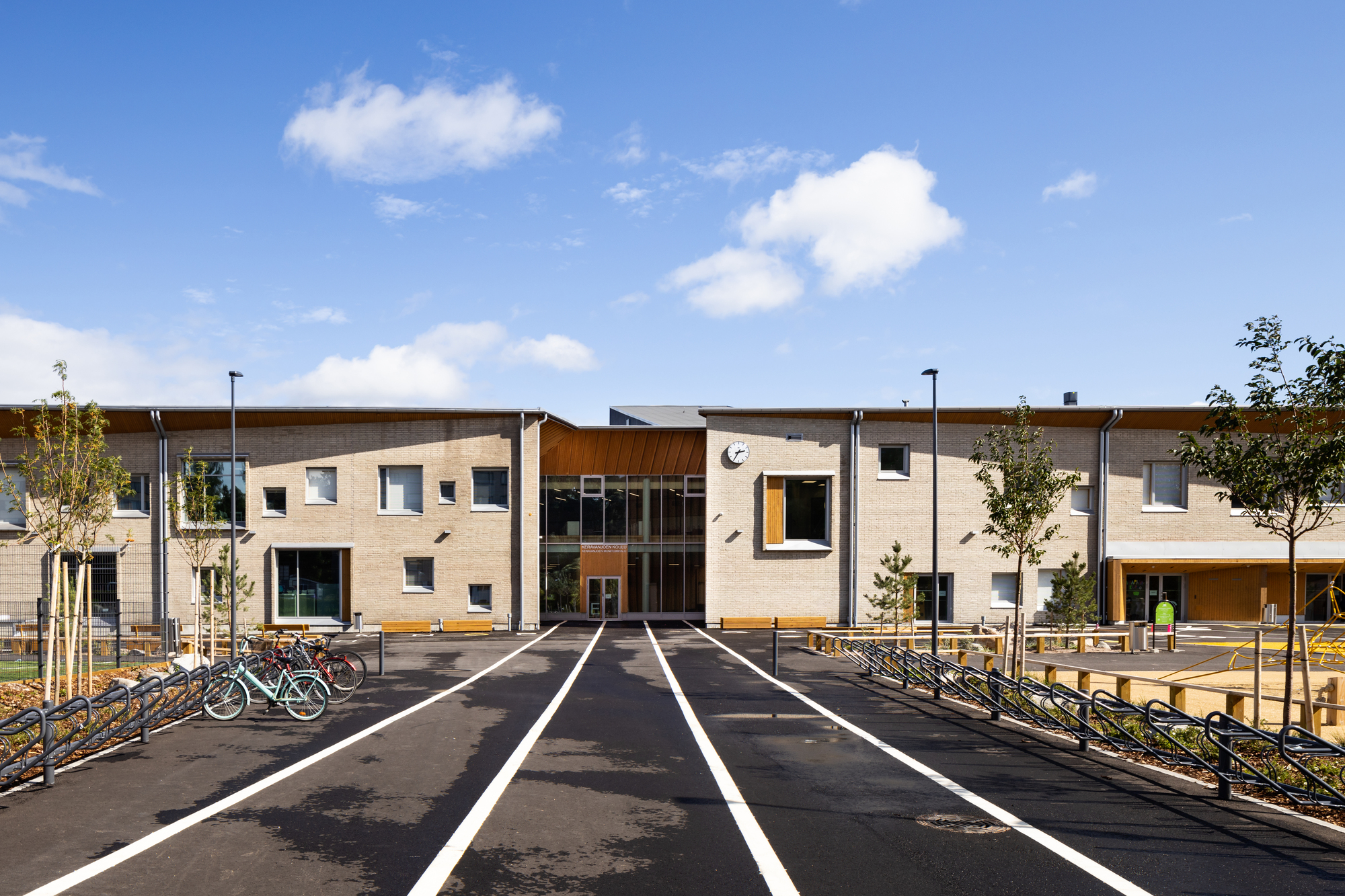 Frontal view of the entrance courtyard with cream brick facades and timber cladding under a blue sky
