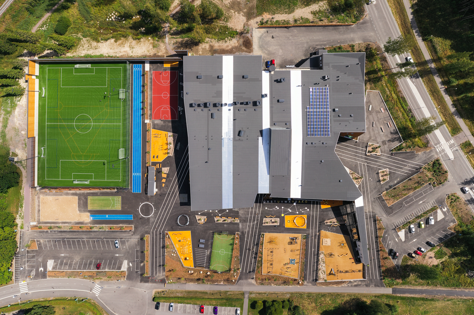 Top-down drone view showing the roofscape with sports courts and colorful play areas below