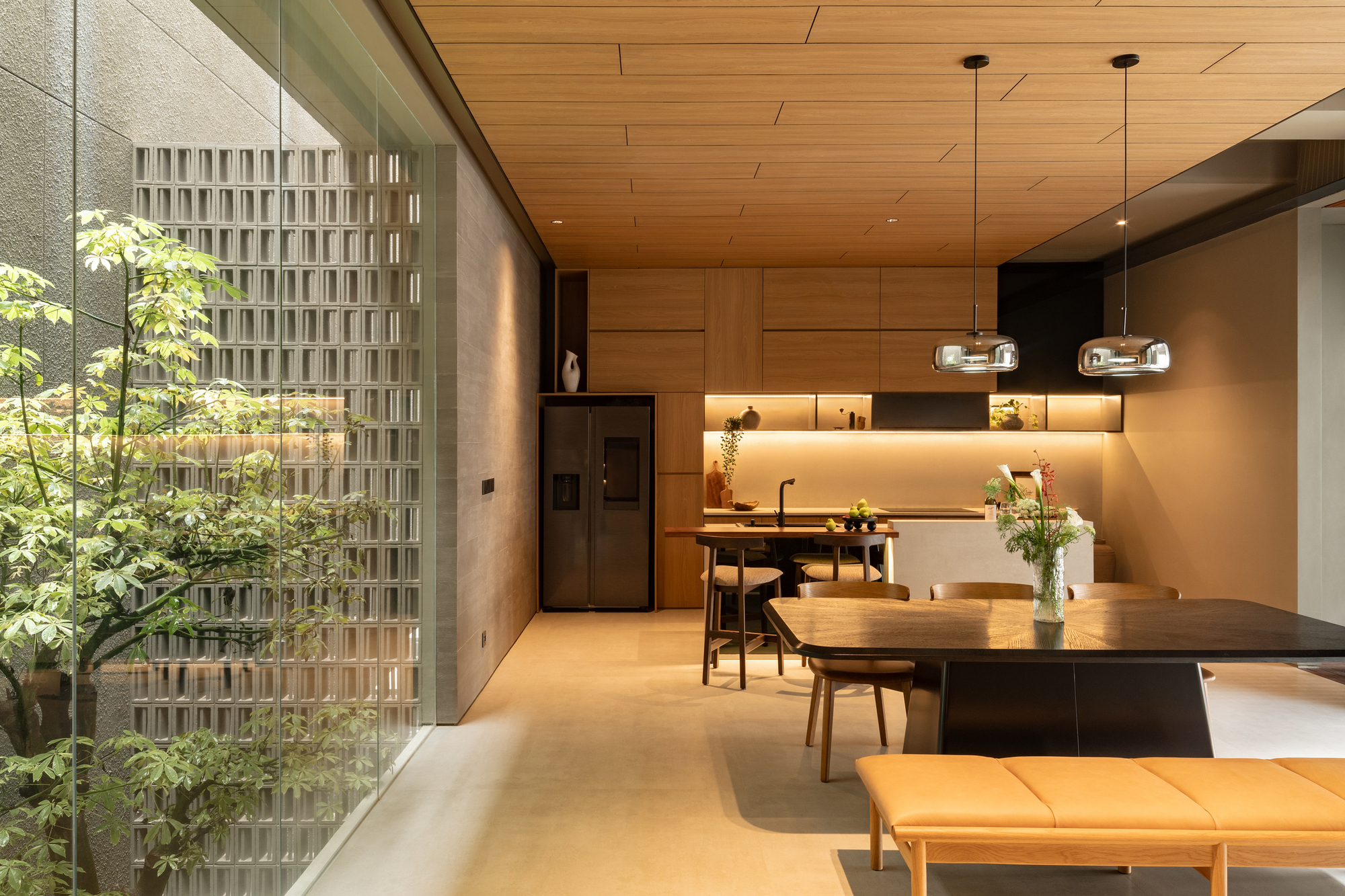 Open-plan dining and living space with timber ceiling and courtyard view through perforated screen wall