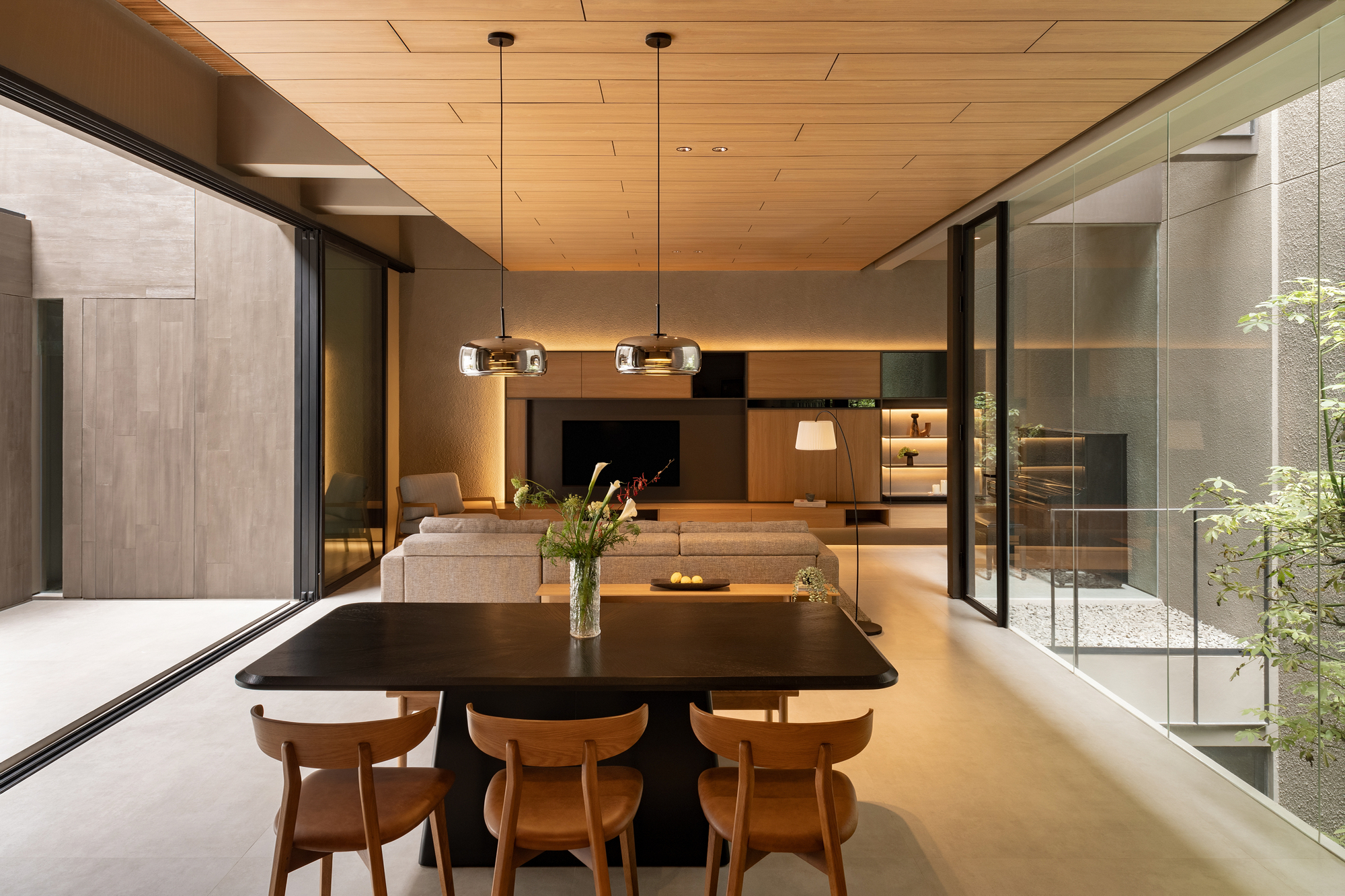 Dining area with glazed courtyard walls framing planted beds and gravel beyond the timber-clad interior