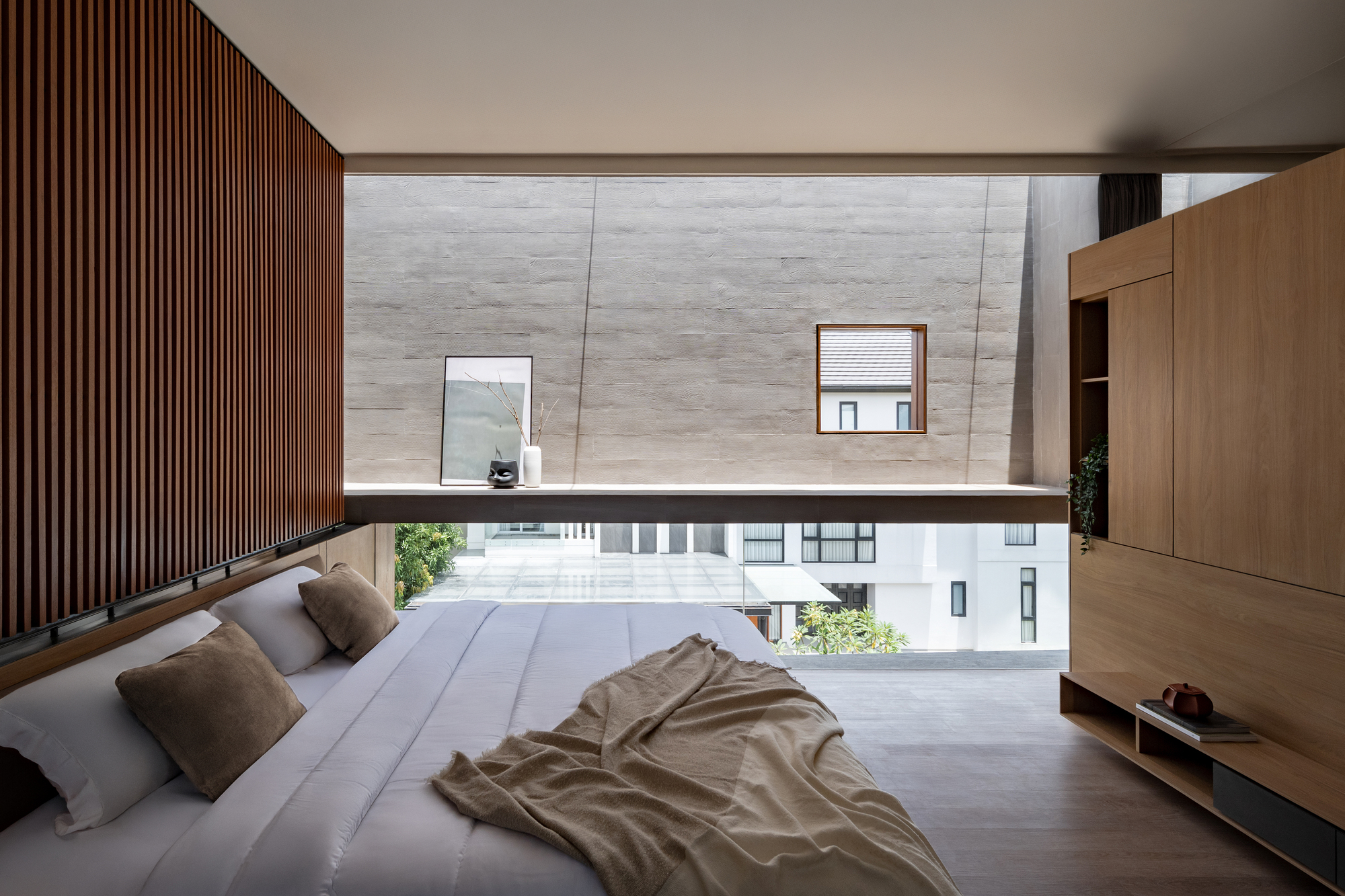 Upper-level bedroom with slatted timber wall and horizontal window overlooking neighboring rooftops and greenery