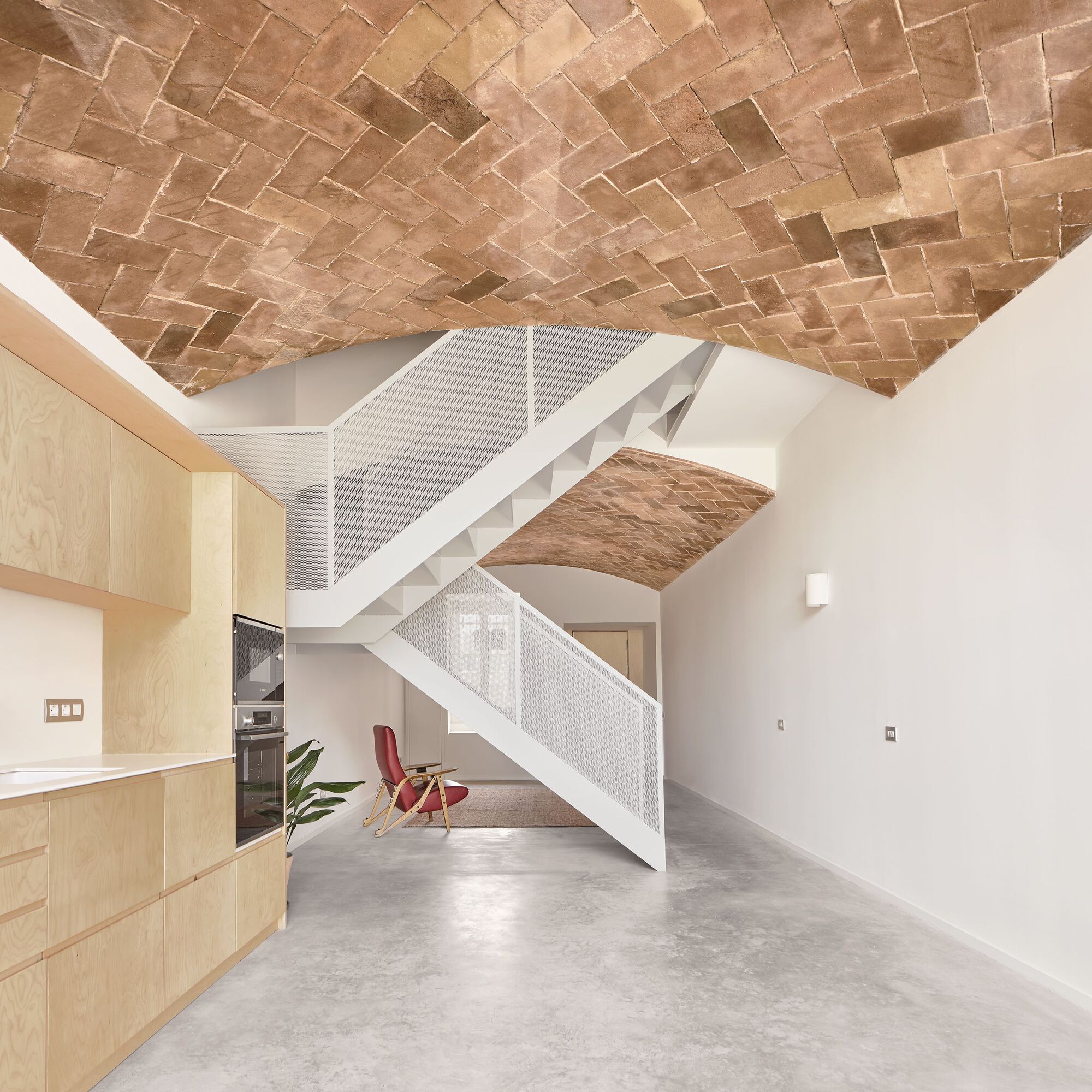 Open living space with herringbone brick vault ceiling, light wood kitchen and white steel staircase