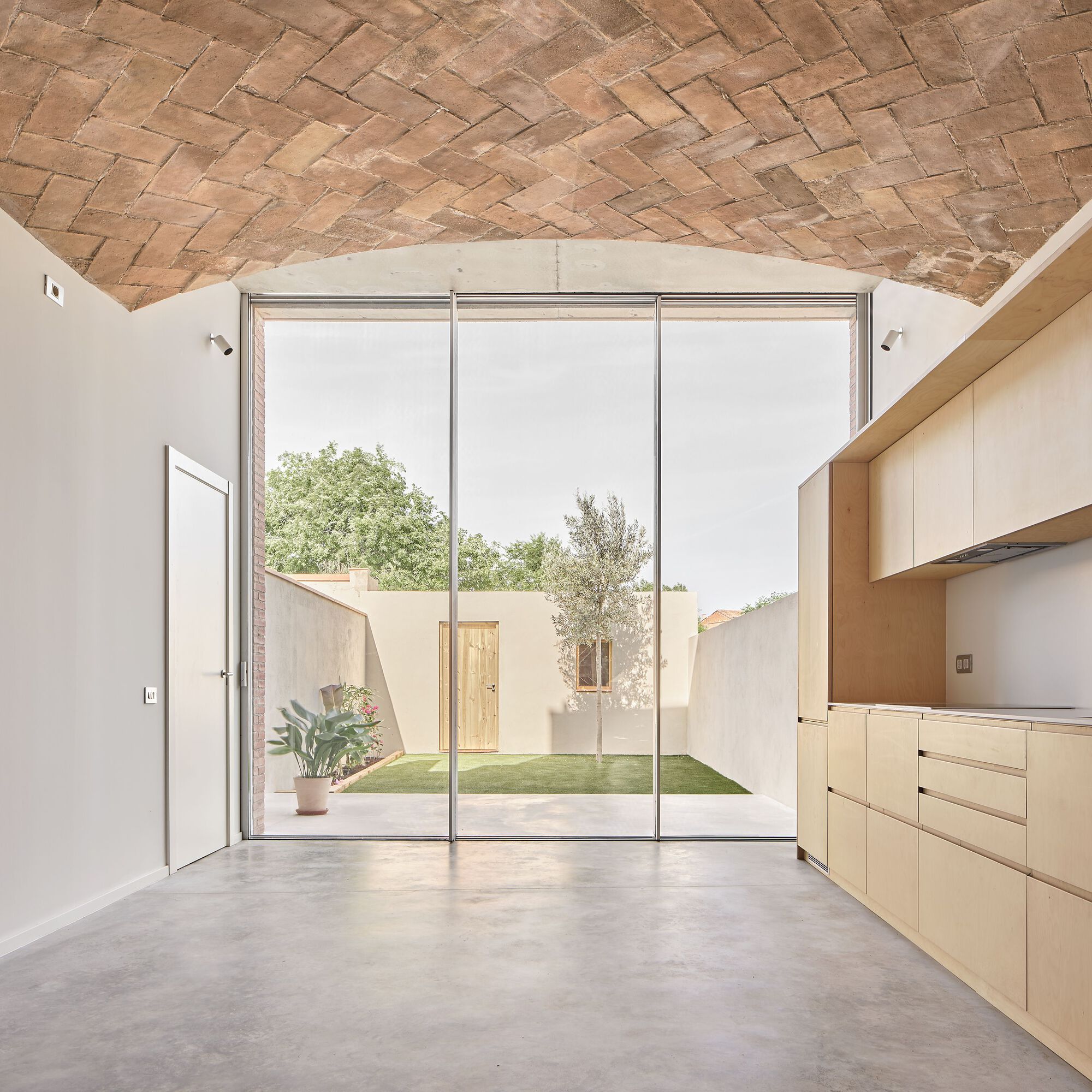 Full-height glazed doors opening to a courtyard garden under a herringbone brick vaulted ceiling