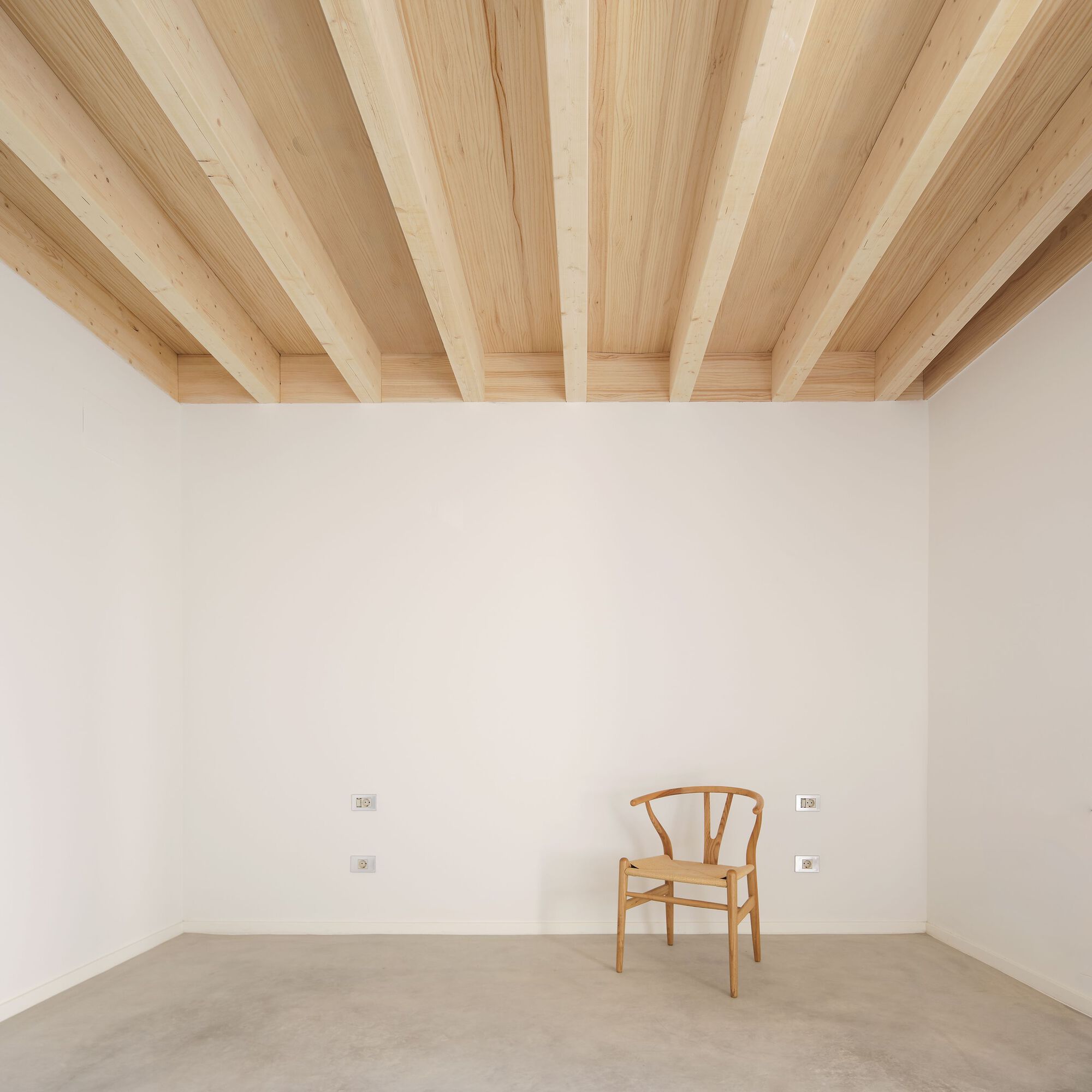 Interior corner with exposed timber beam ceiling and a single wooden chair on polished concrete floor