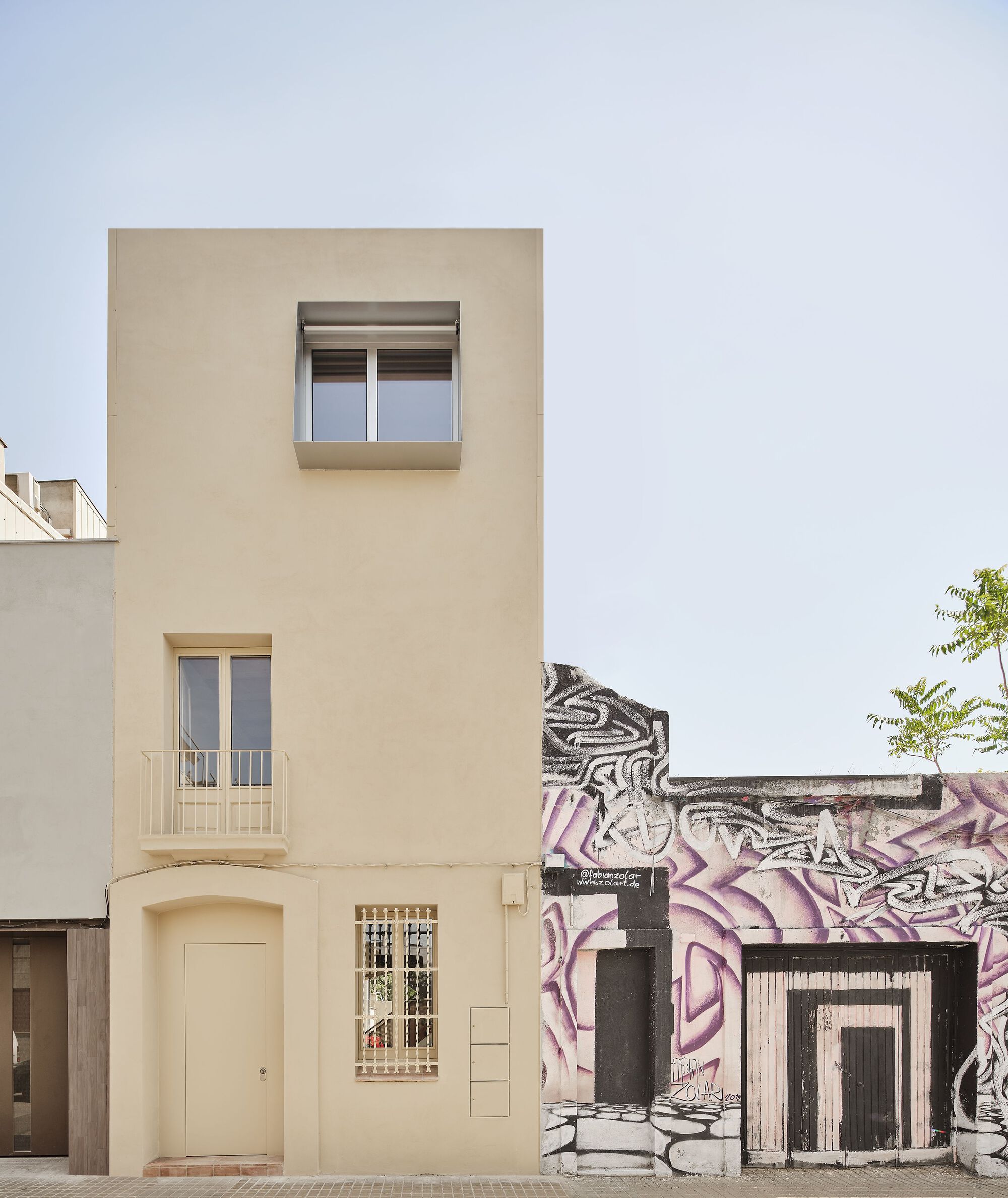 Narrow cream facade with arched entry and square windows beside a graffitied neighboring building