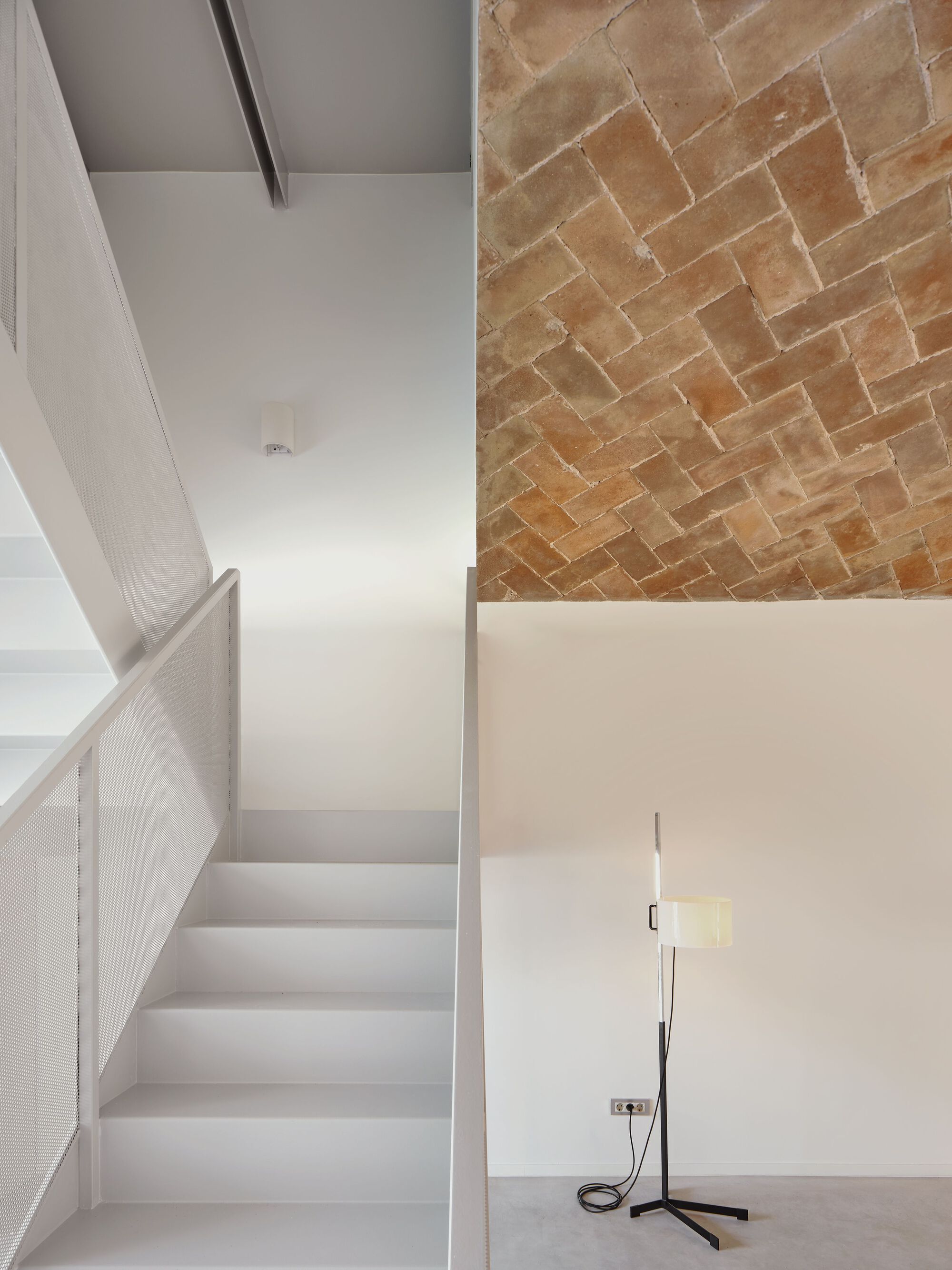 Stairwell with perforated metal balustrade where white plaster ceiling meets herringbone brick vault