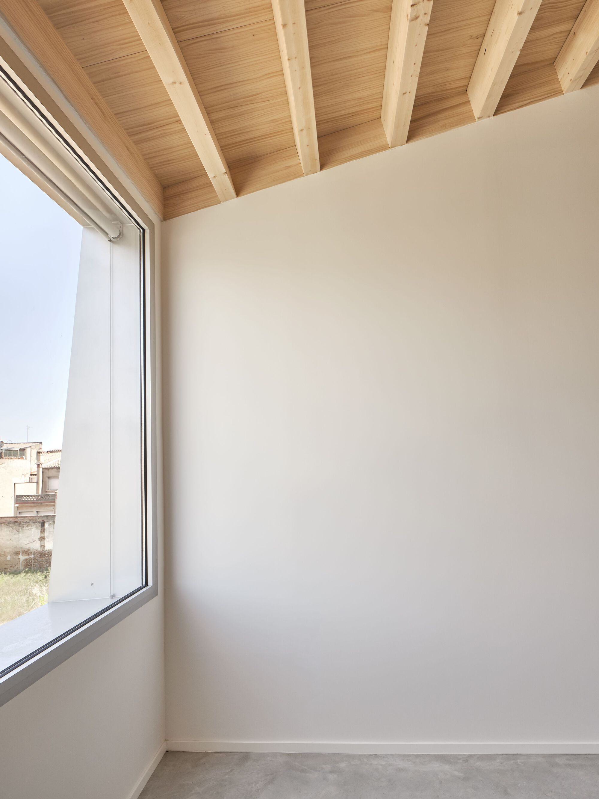 Corner room with exposed timber beams and a tall window overlooking rooftops under overcast sky