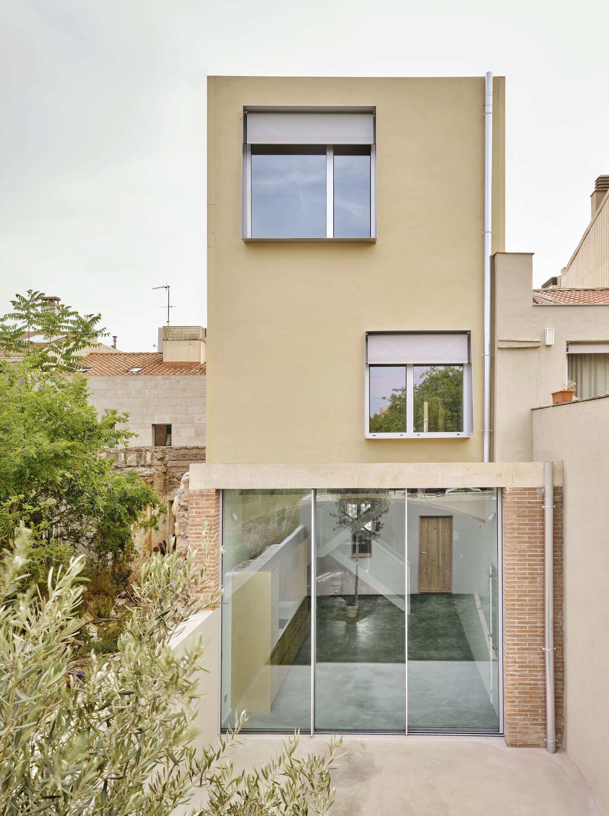 Street view of cream stucco facade with protruding windows and full-height glazed ground floor entry with brick surround