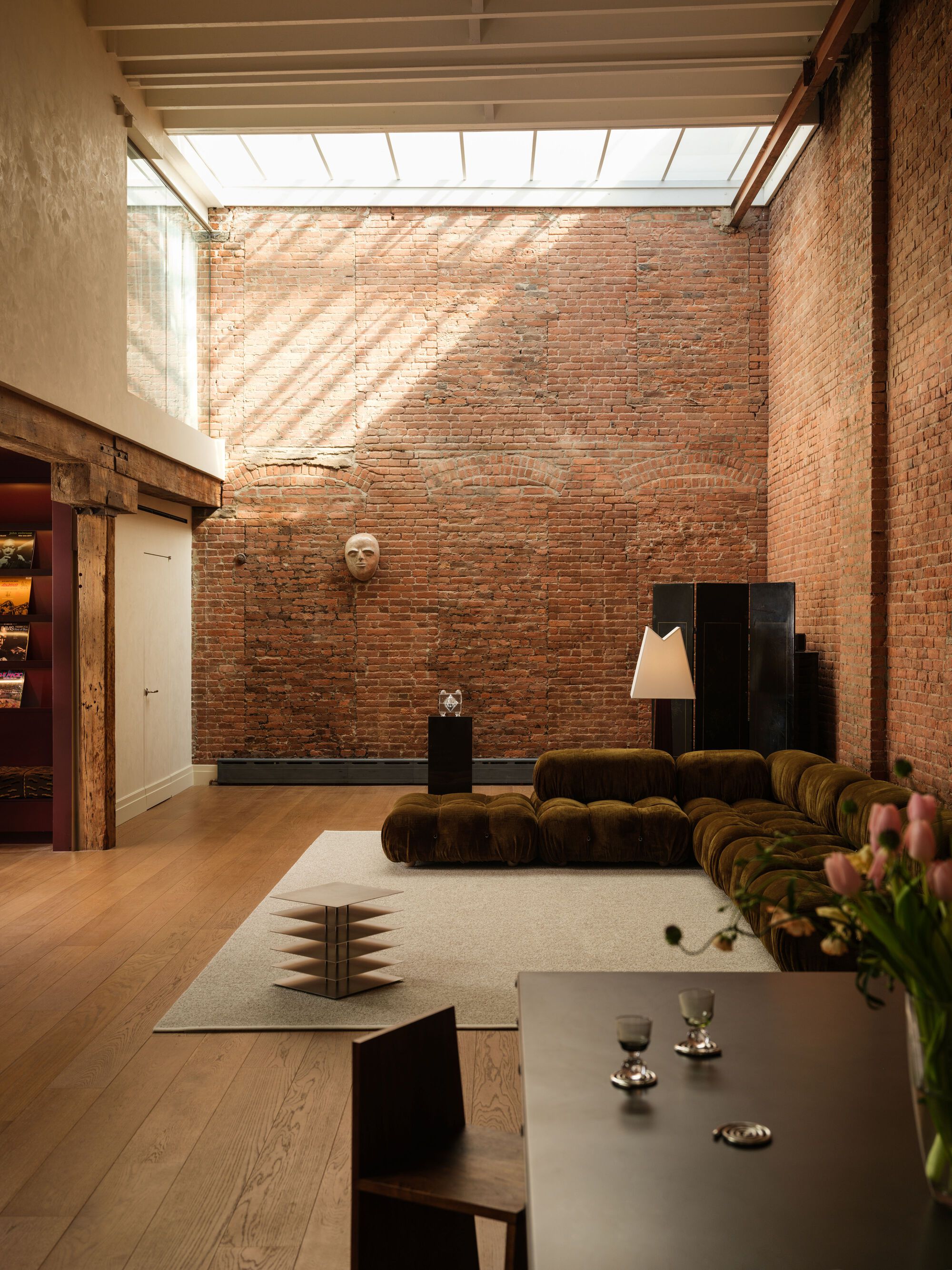 Double-height room with exposed brick wall lit by clerestory skylight above