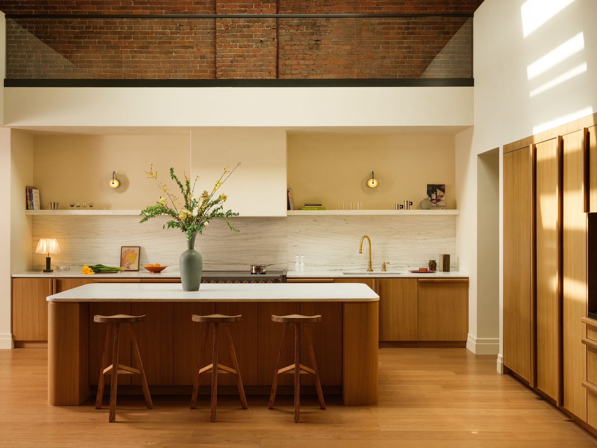 Kitchen island with walnut cabinetry and white countertop beneath exposed brick ceiling beams
