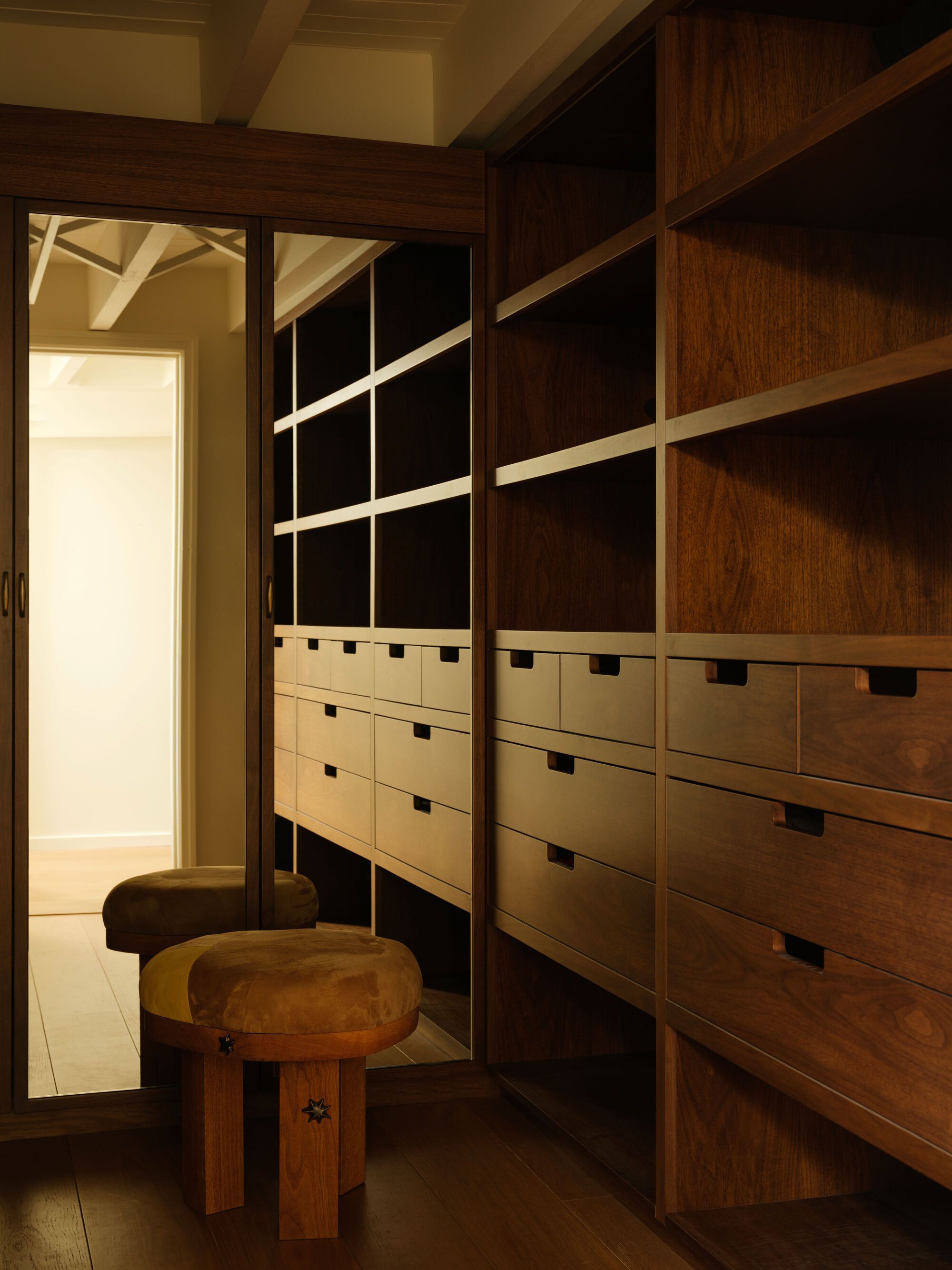 Custom closet with two-tone wood shelving, drawer banks, and angular display rods under a coffered ceiling