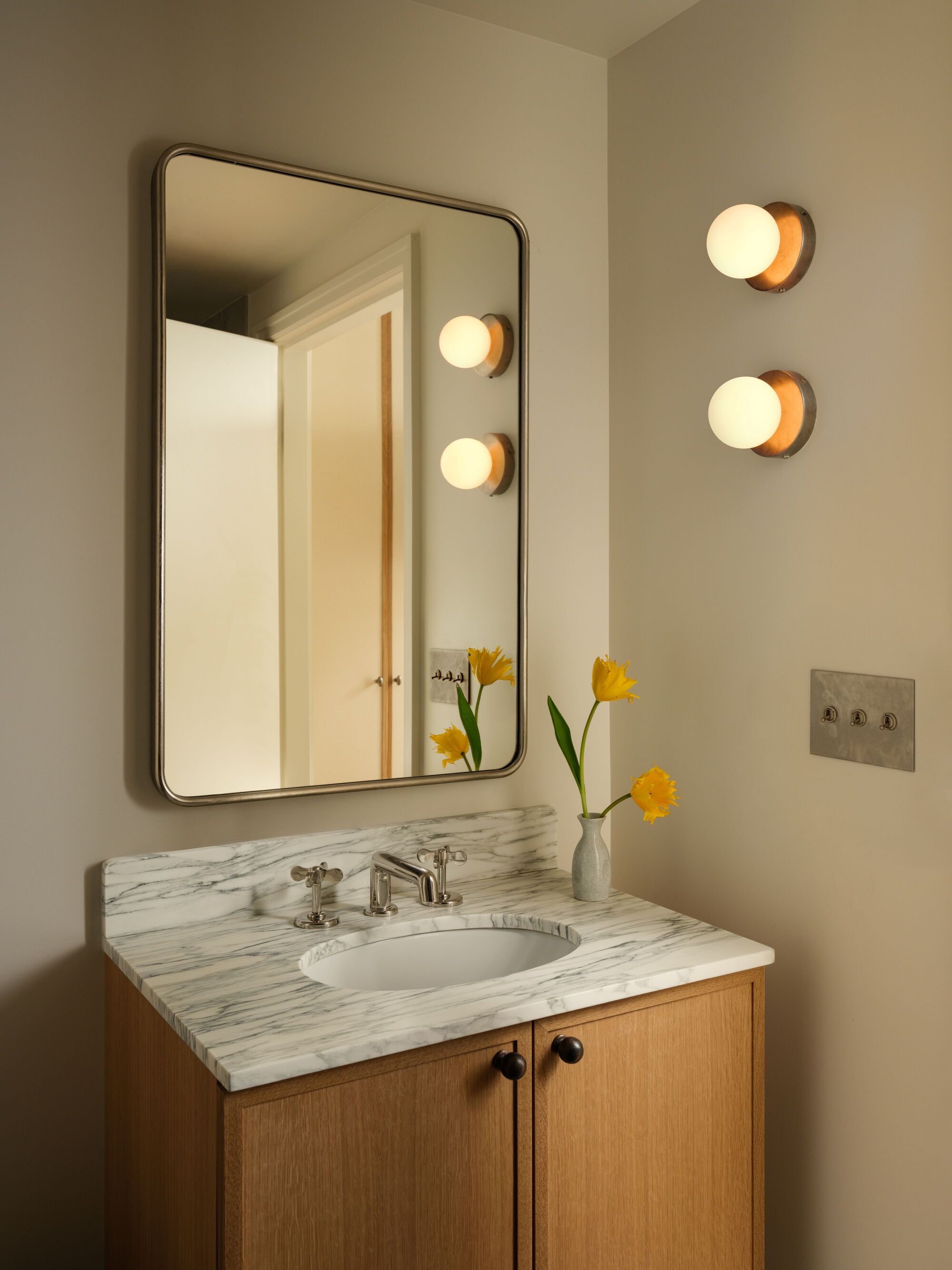 Bathroom mirror with rounded corners above marble vanity counter with yellow flowers in glass vase