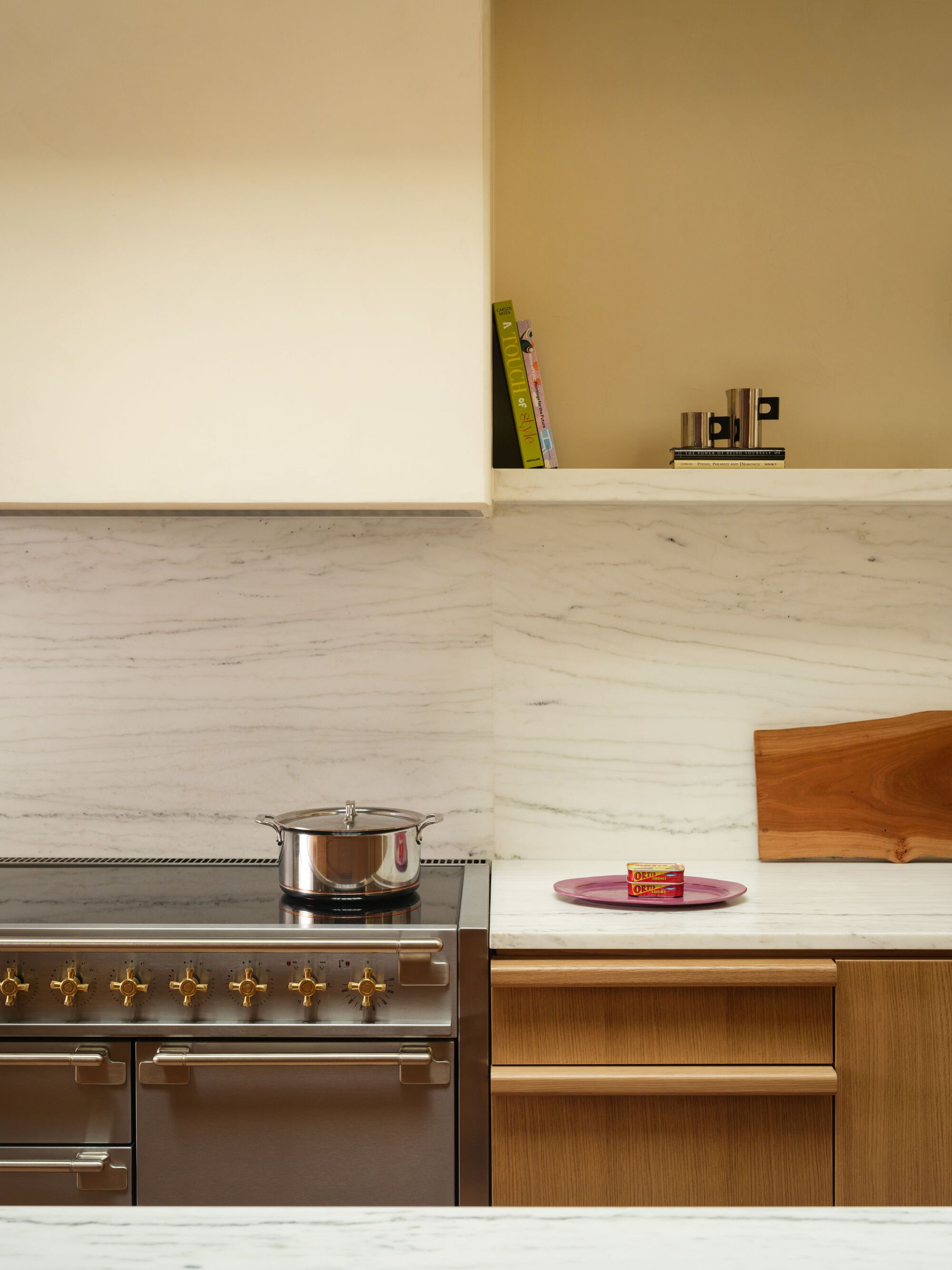 Kitchen counter with white marble backsplash, oak cabinetry and stainless range with brass knobs