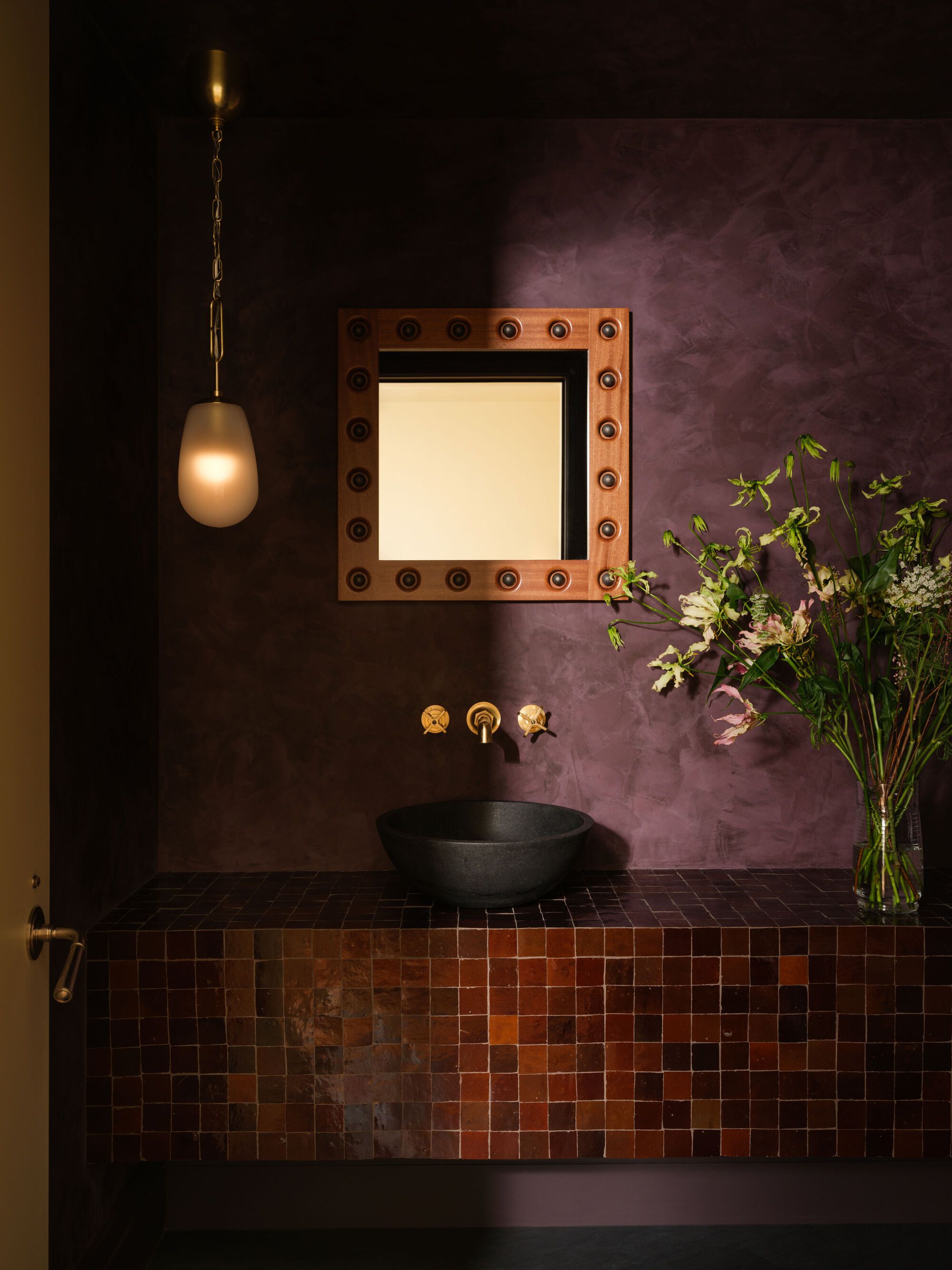 Powder room vanity clad in variegated copper tile with purple plaster walls and pendant light