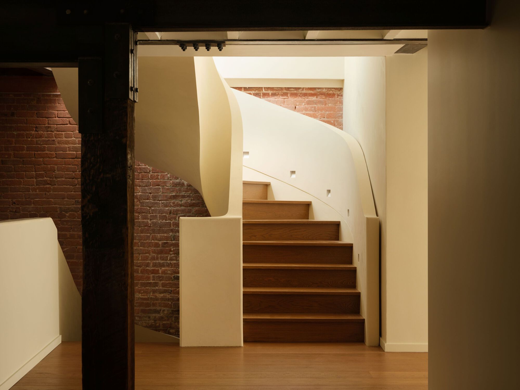 View through a dark timber doorframe to the curved staircase with cream plaster walls