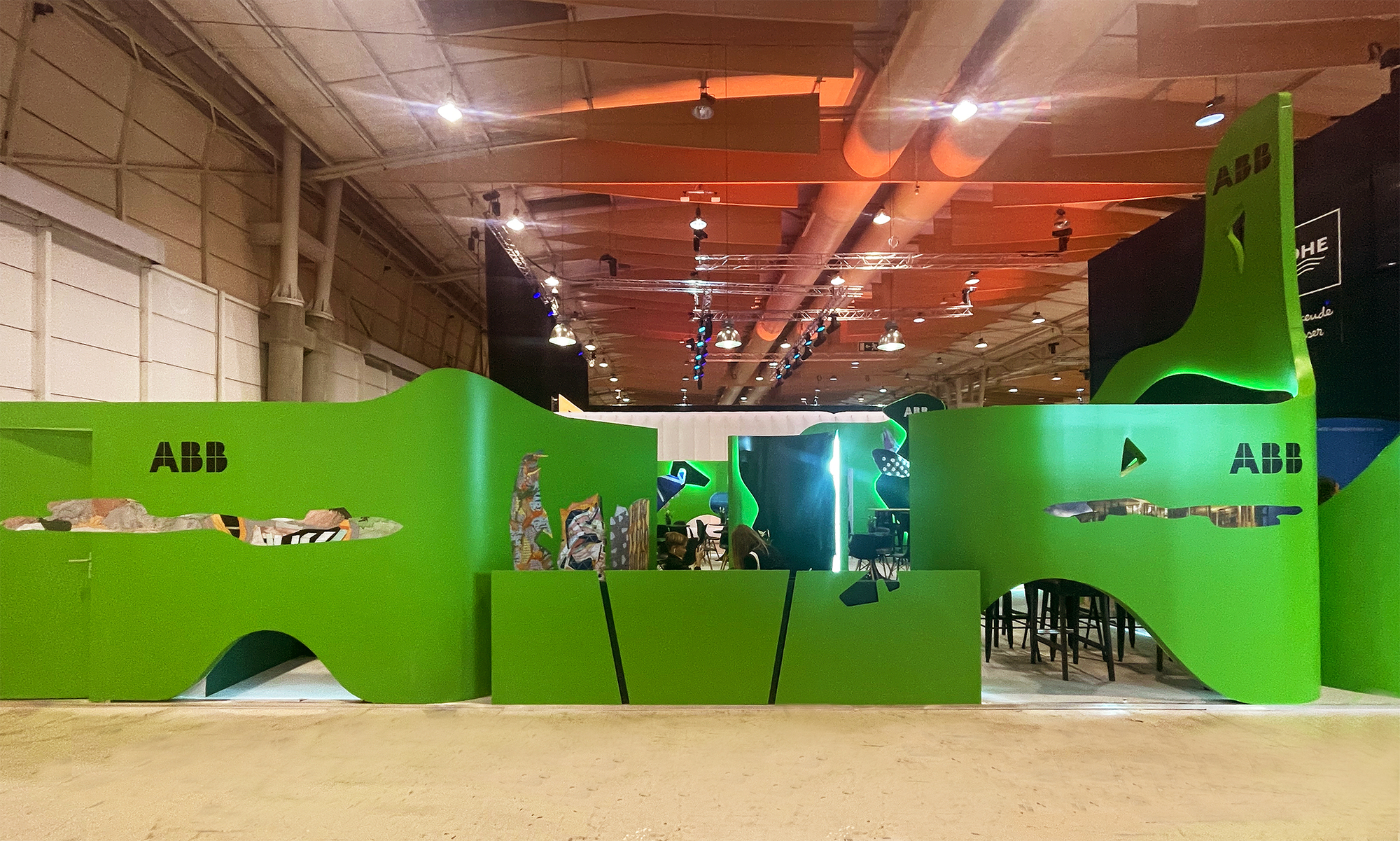 Bright green undulating exhibition walls with cutout openings under an exposed industrial ceiling