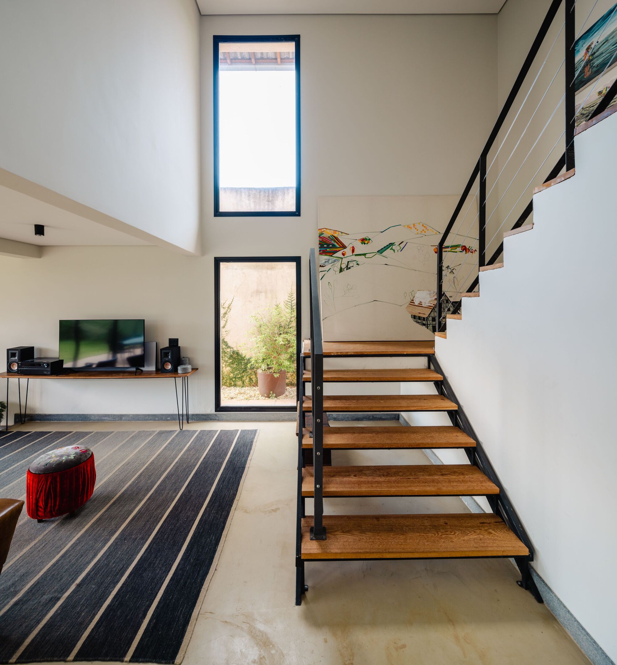 Double-height living room with open timber and steel staircase overlooking a striped rug and media console