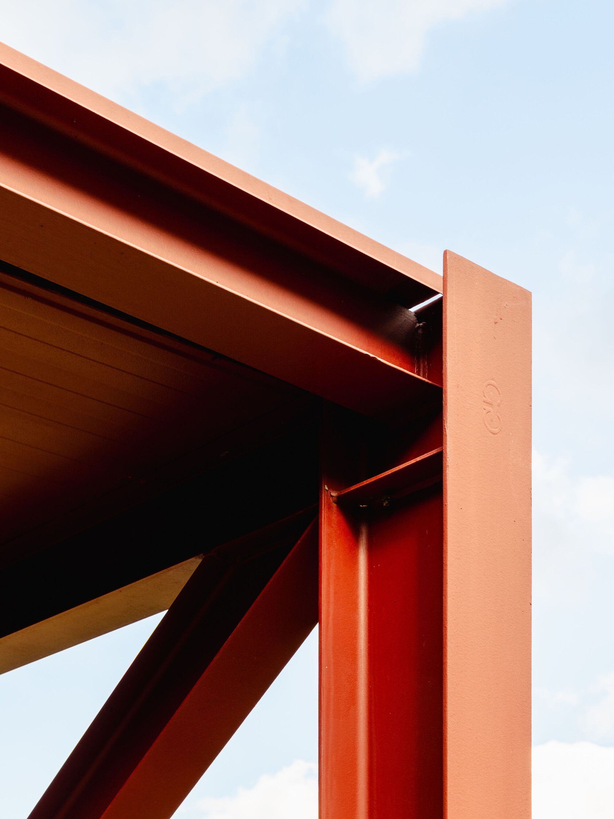 Close-up of painted steel beam connection with diagonal bracing against a cloudy sky